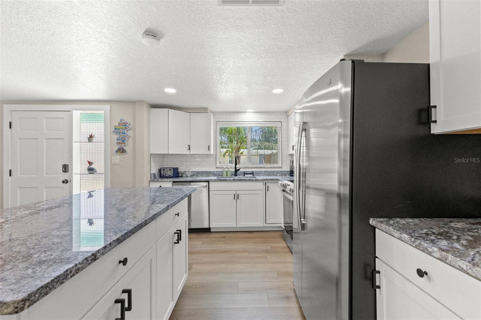 201 SOUTH STREET, Palm Harbor, FL 34683 Another view highlights the kitchens extensive cabinetry, stainless steel appliances, granite surfaces, and luxury vinyl plank flooring.