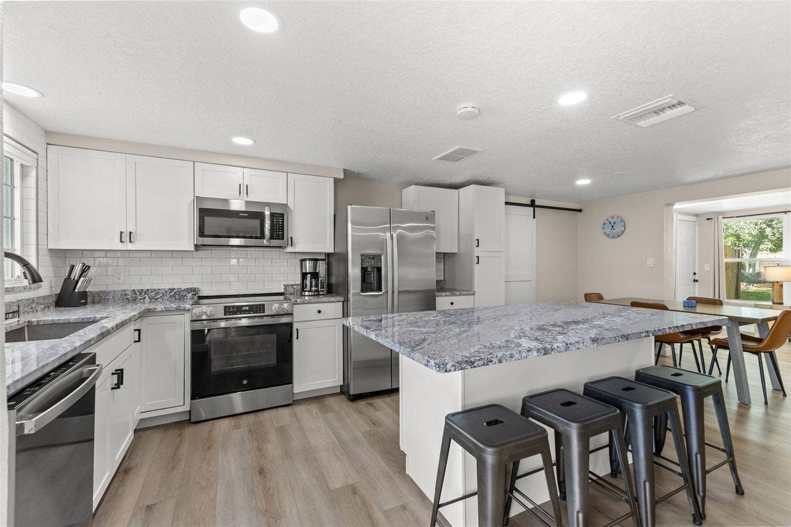 201 SOUTH STREET, Palm Harbor, FL 34683 Renovated kitchen with white cabinetry, granite countertops, stainless steel appliances, and an oversized island with seating for four.