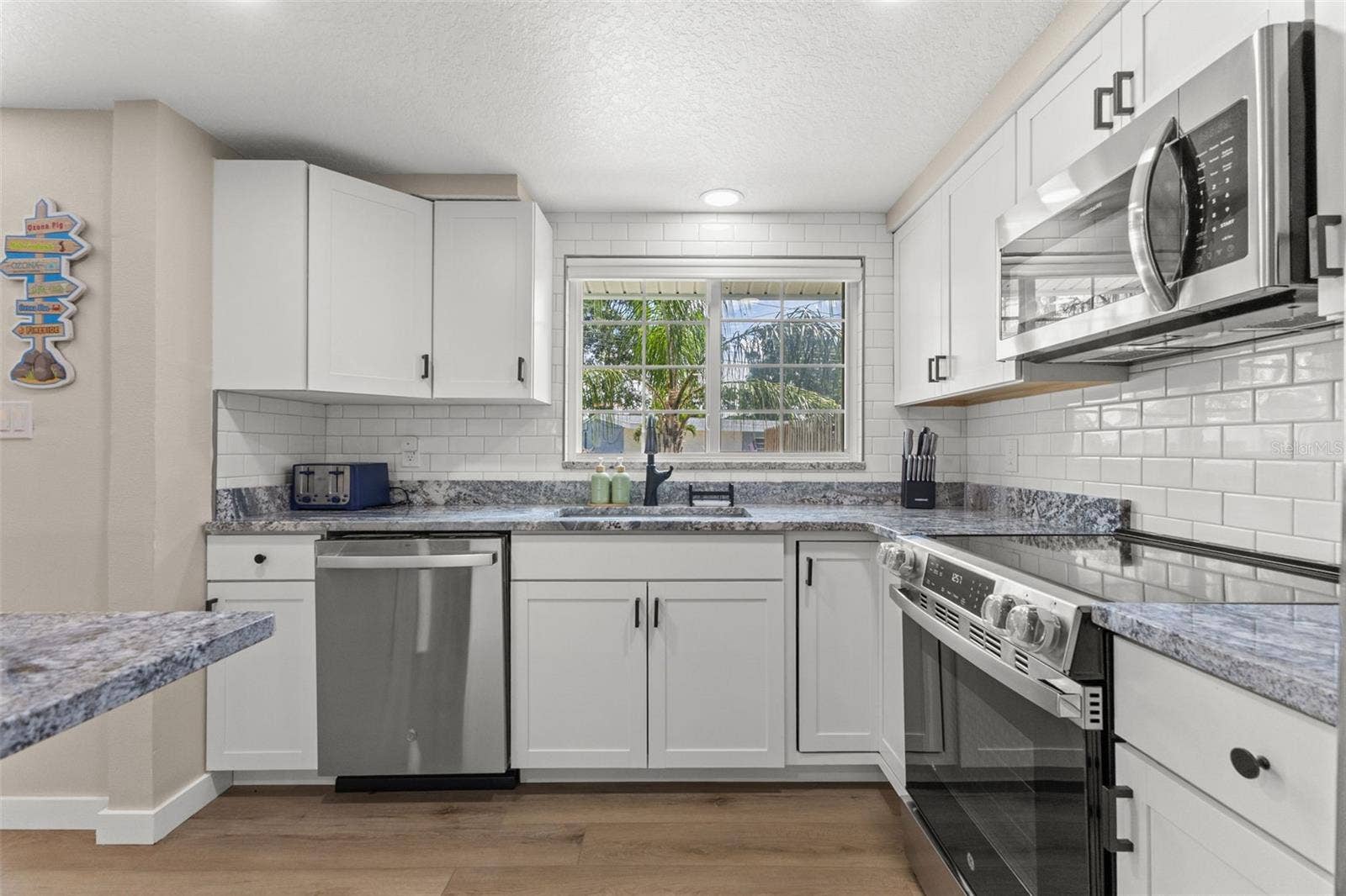 201 SOUTH STREET, Palm Harbor, FL 34683 White cabinetry, granite countertops, subway tile backsplash, stainless steel appliances, and a window above the kitchen sink.