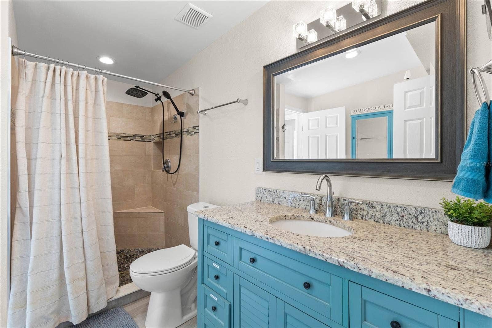 The updated second bath features a turquoise vanity with granite countertop, framed mirror, modern lighting, and a tiled walk-in shower with built-in bench, rainfall showerhead, and handheld sprayer.