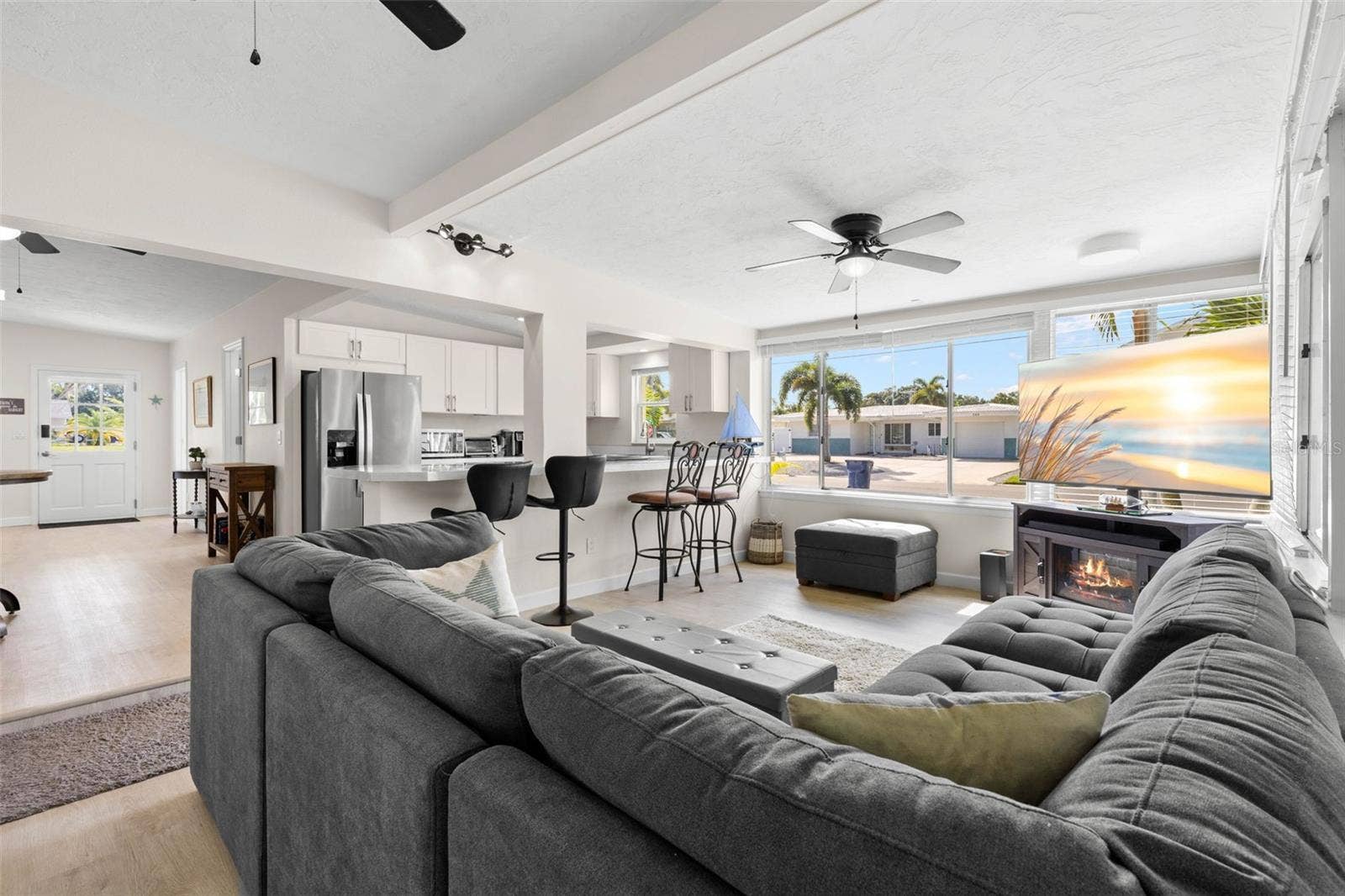 Expansive windows flood the living room with natural light, while the open connection to the updated kitchen, breakfast bar, ceiling fan, and fireplace creates a bright, comfortable gathering space.