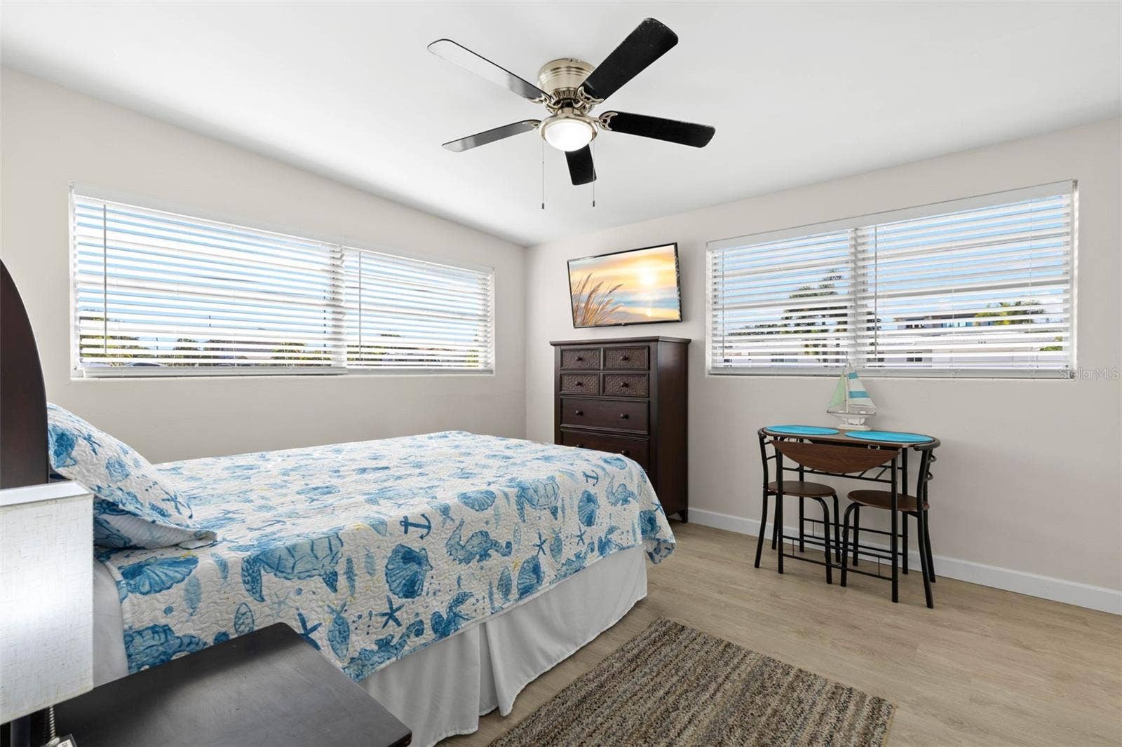 The third bedroom features two walls of windows, a ceiling fan, neutral tones, and luxury vinyl plank flooring (2025), with enough space for both sleeping and a small sitting or study area.