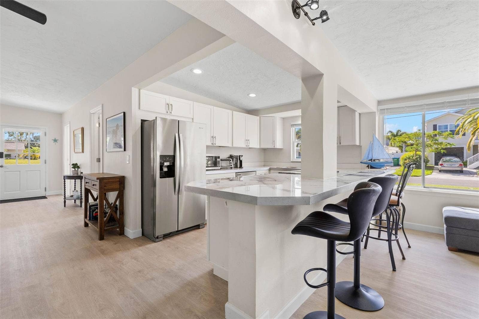 The updated kitchen (2025) pairs crisp white cabinetry and stainless steel appliances with expansive counter space and a wraparound breakfast bar that adds both seating and everyday functionality.