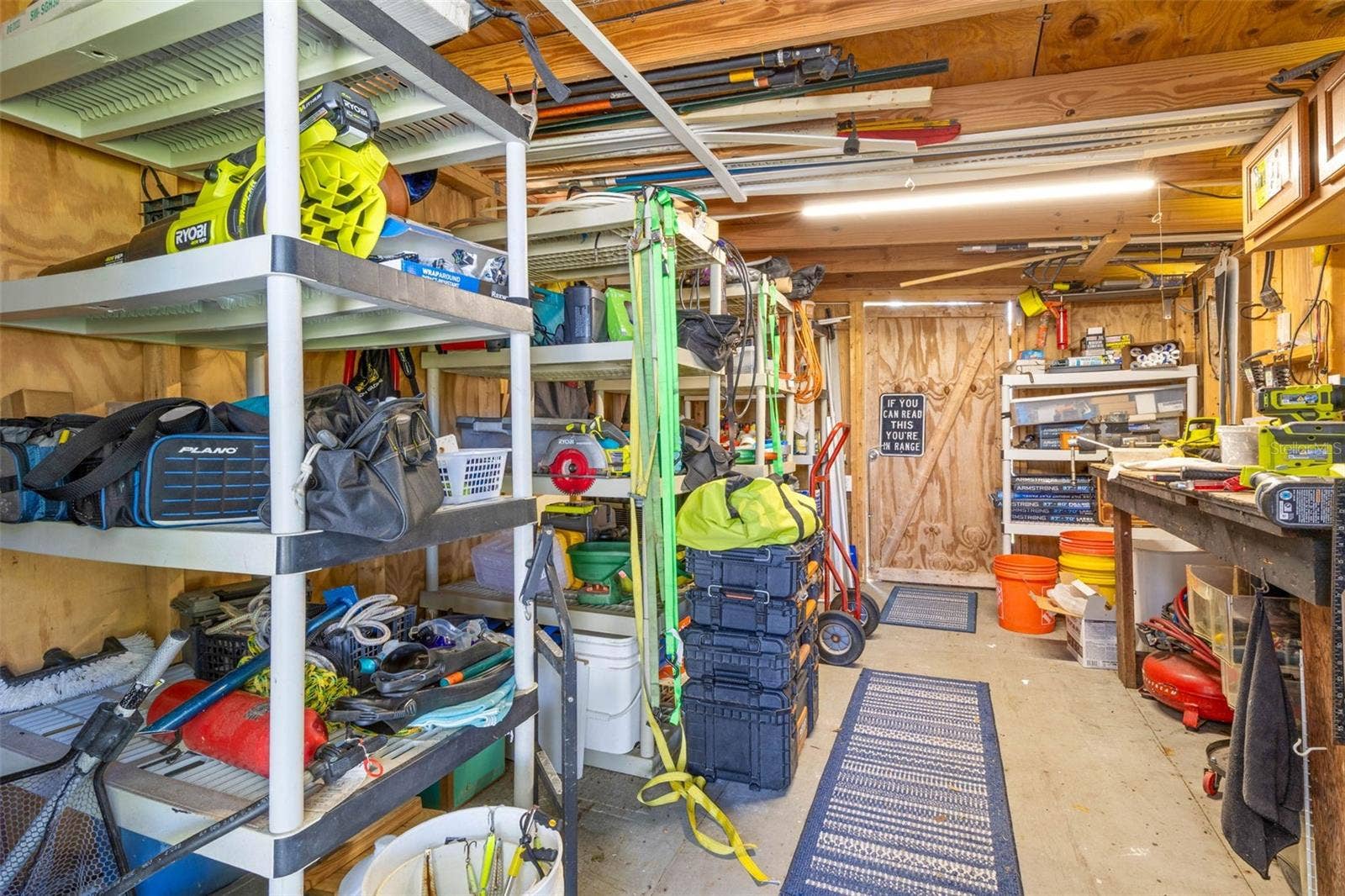 A dedicated workshop offers serious utility with abundant shelving, a long workbench, overhead storage, lighting, and plenty of room for tools, fishing gear, projects, and everyday equipment.