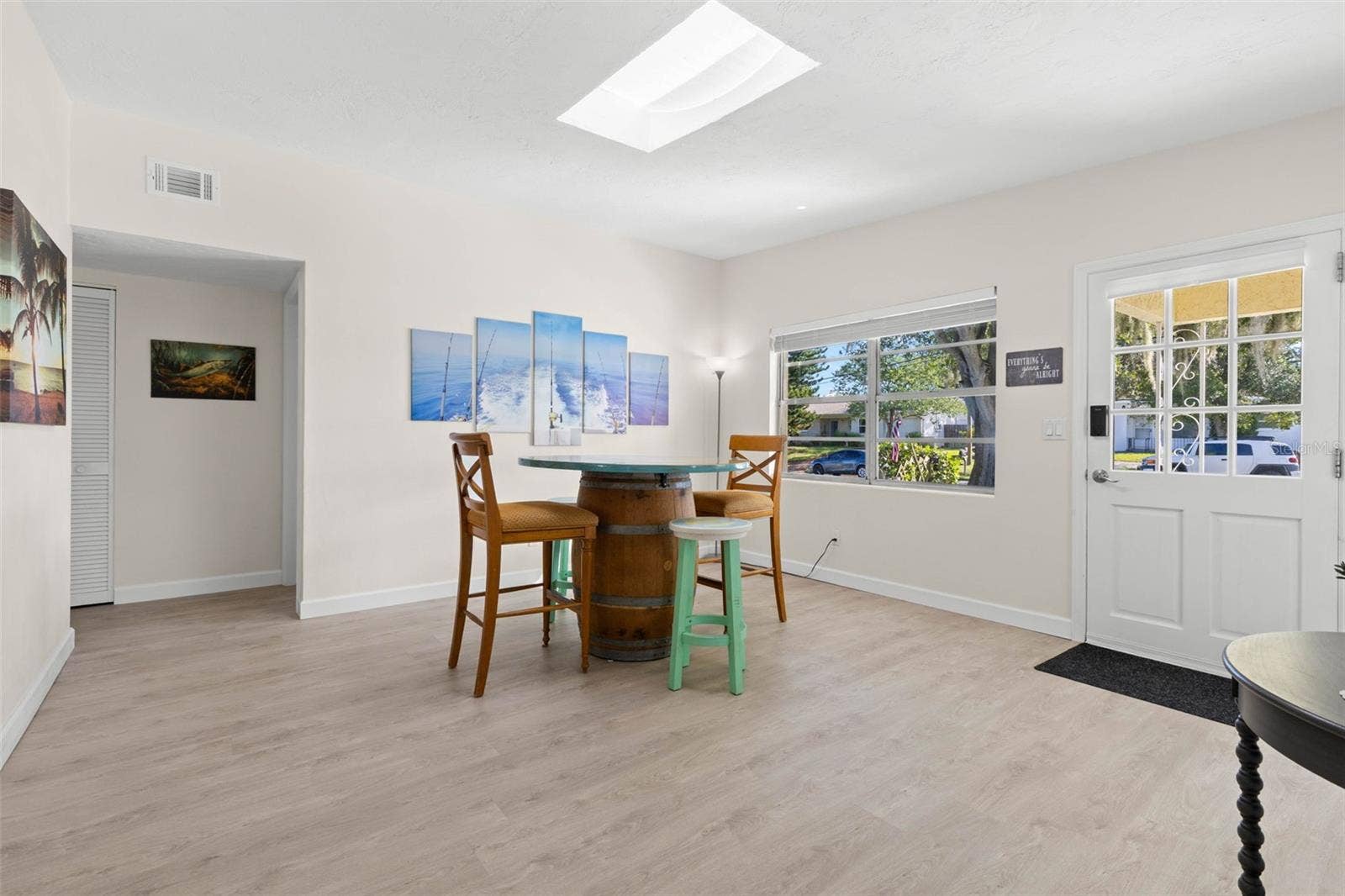 Step inside to a bright, open dining area with 2025 luxury vinyl plank flooring, a skylight overhead, and broad front windows that fill the space with natural light.