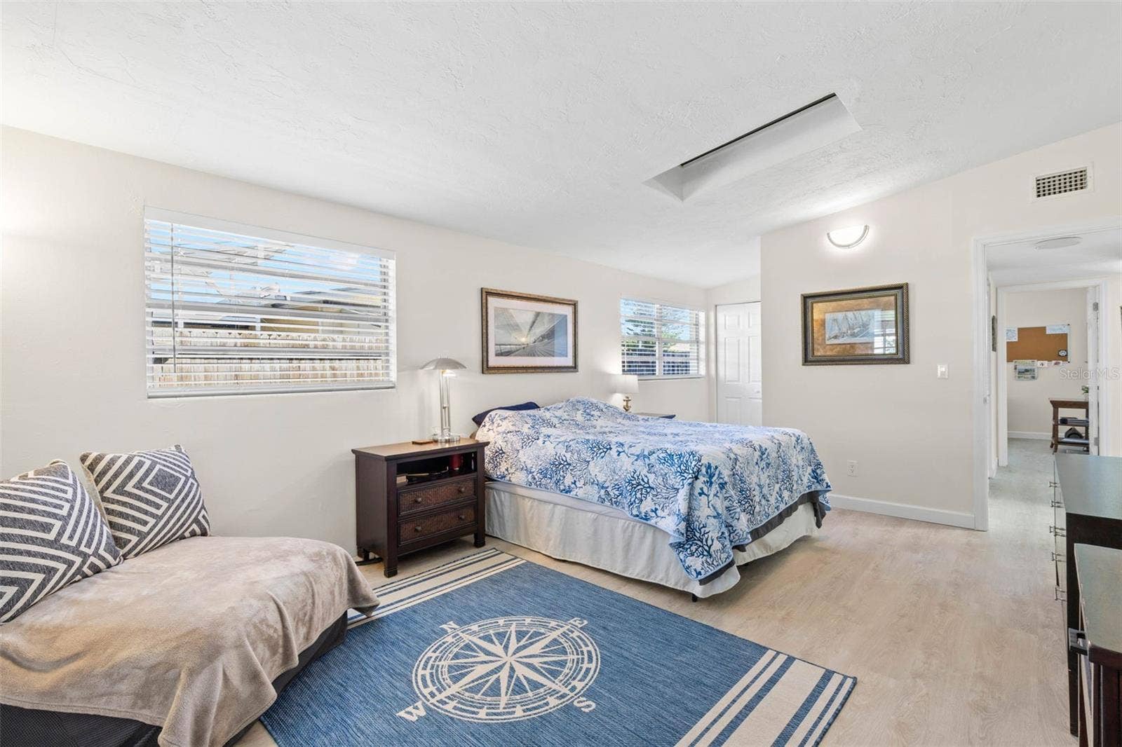 The spacious primary bedroom easily accommodates a king-size bed and a dedicated sitting area, with multiple windows, a skylight, neutral tones, and luxury vinyl plank flooring (2025) adding to the bright, open feel.
