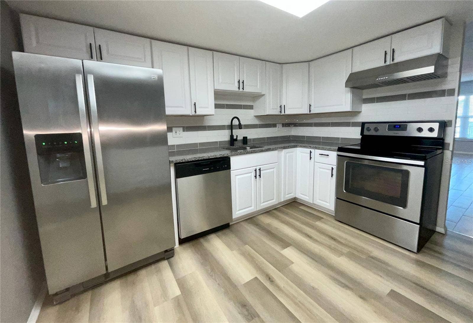 Kitchen sink area with frig, dishwasher and range.