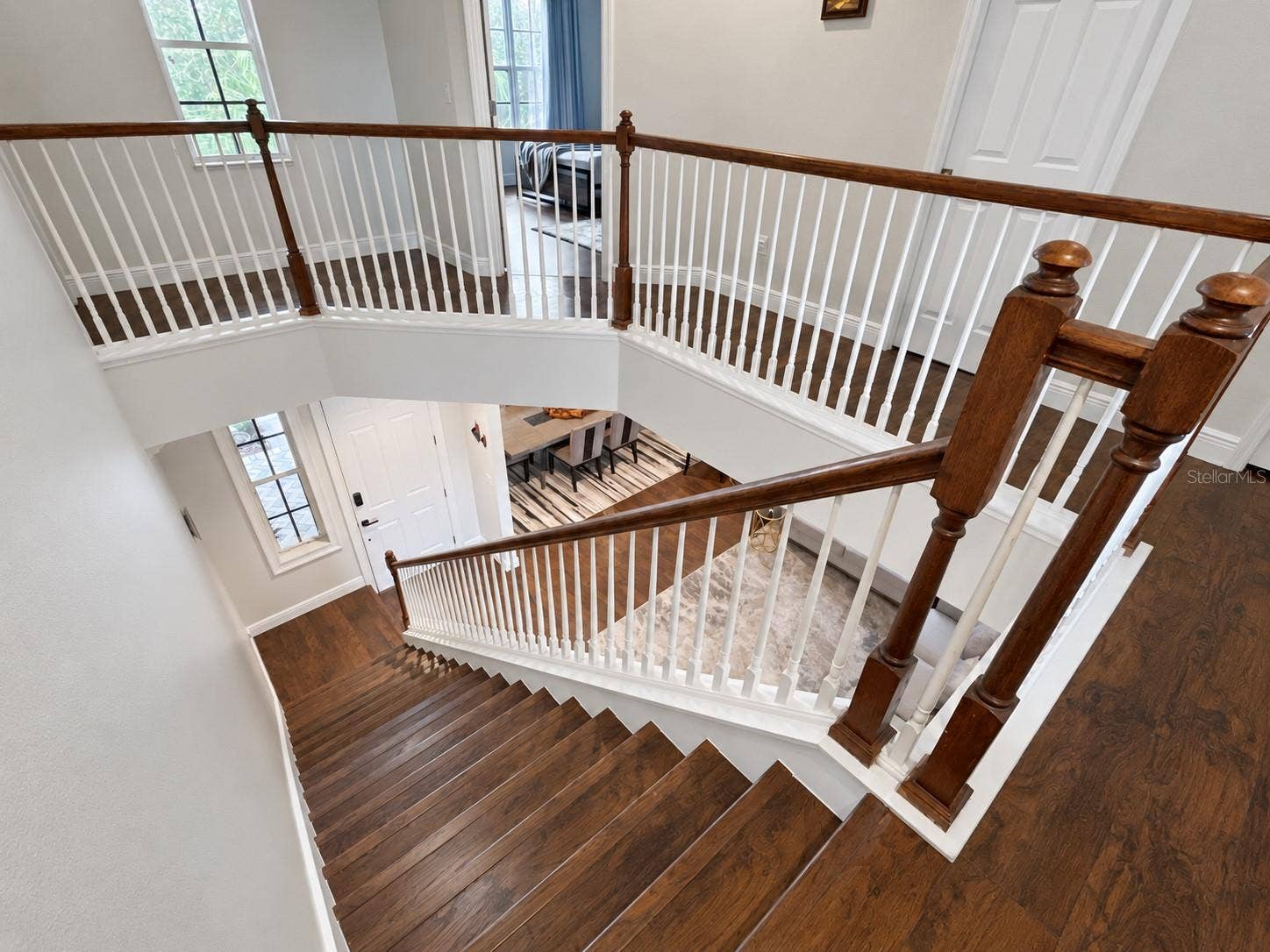 An open staircase with wood treads, white balusters, and a matching wood handrail connects the two levels. The upper landing overlooks the entrance, with tall windows bringing light into the circulation spaces.