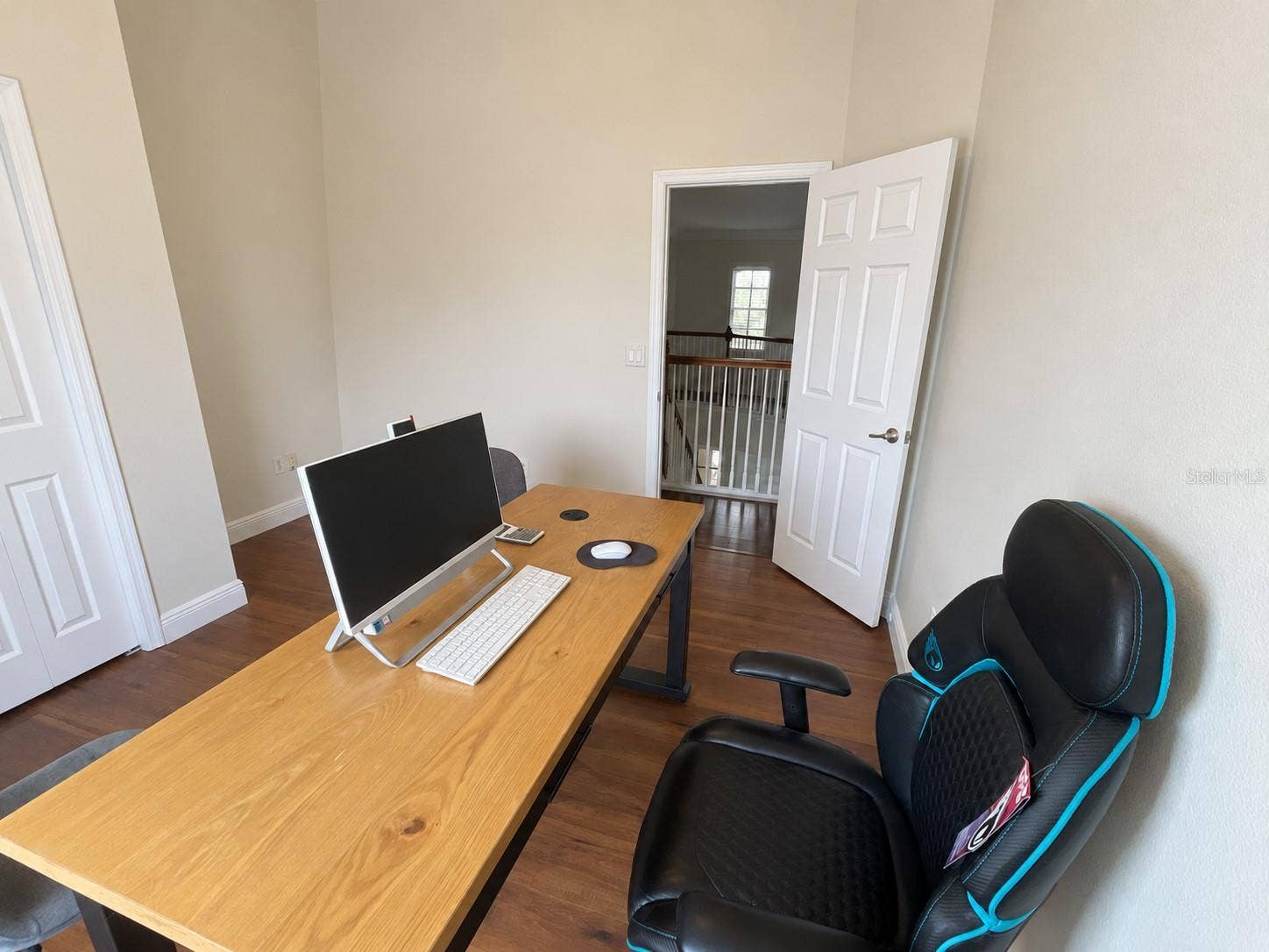 A dedicated office with a large window overlooking the water and ample room for a desk and guest seating. Neutral walls and wood-tone flooring create a simple, comfortable workspace.