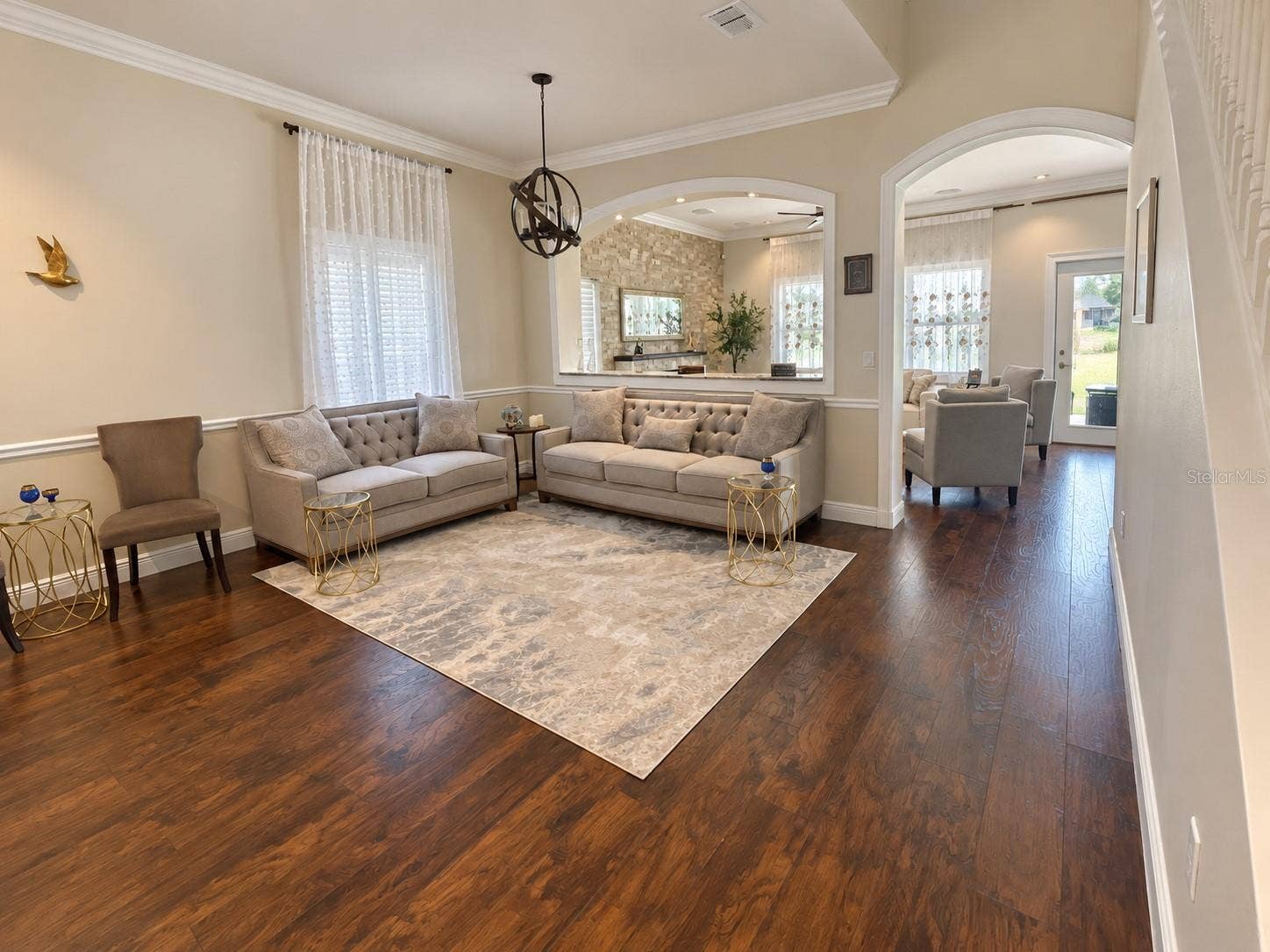 An airy sitting room near the entrance features crown molding, large windows, and an open connection to the formal dining area. Arched openings add character and connect the surrounding spaces.