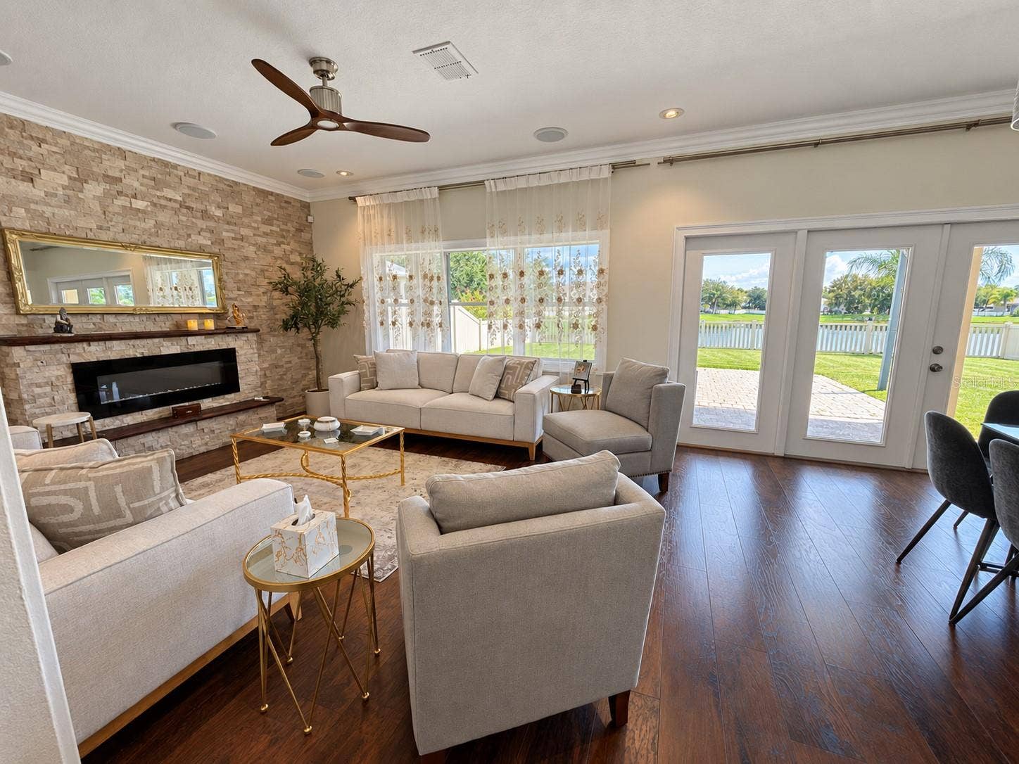 An inviting gathering space centered around a stone accent wall with a fireplace and mantel. Large windows bring in natural light, while the open layout connects easily to the kitchen and breakfast area.