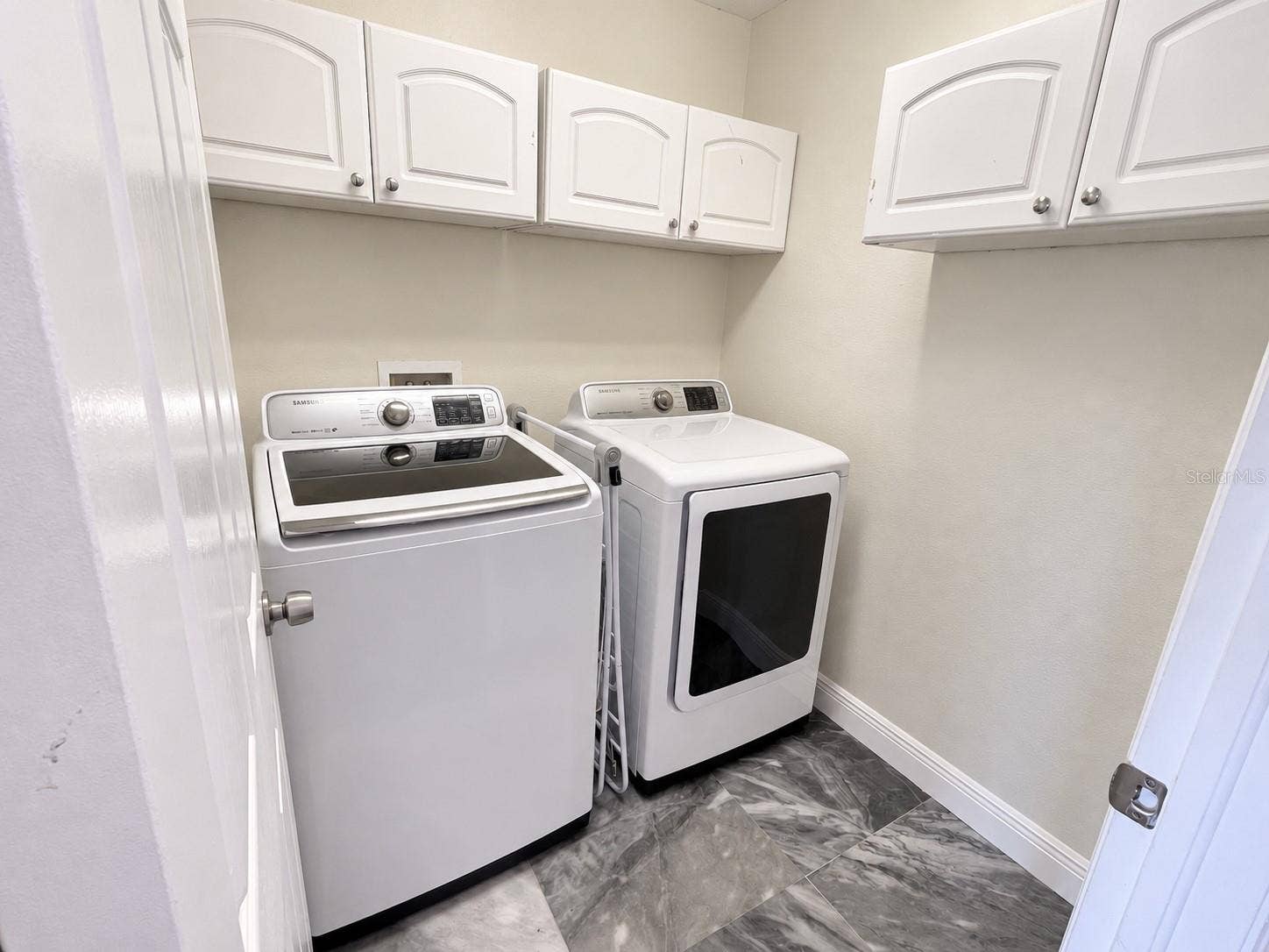 A separate laundry room with side-by-side washer and dryer, overhead storage cabinets, and a tiled floor.