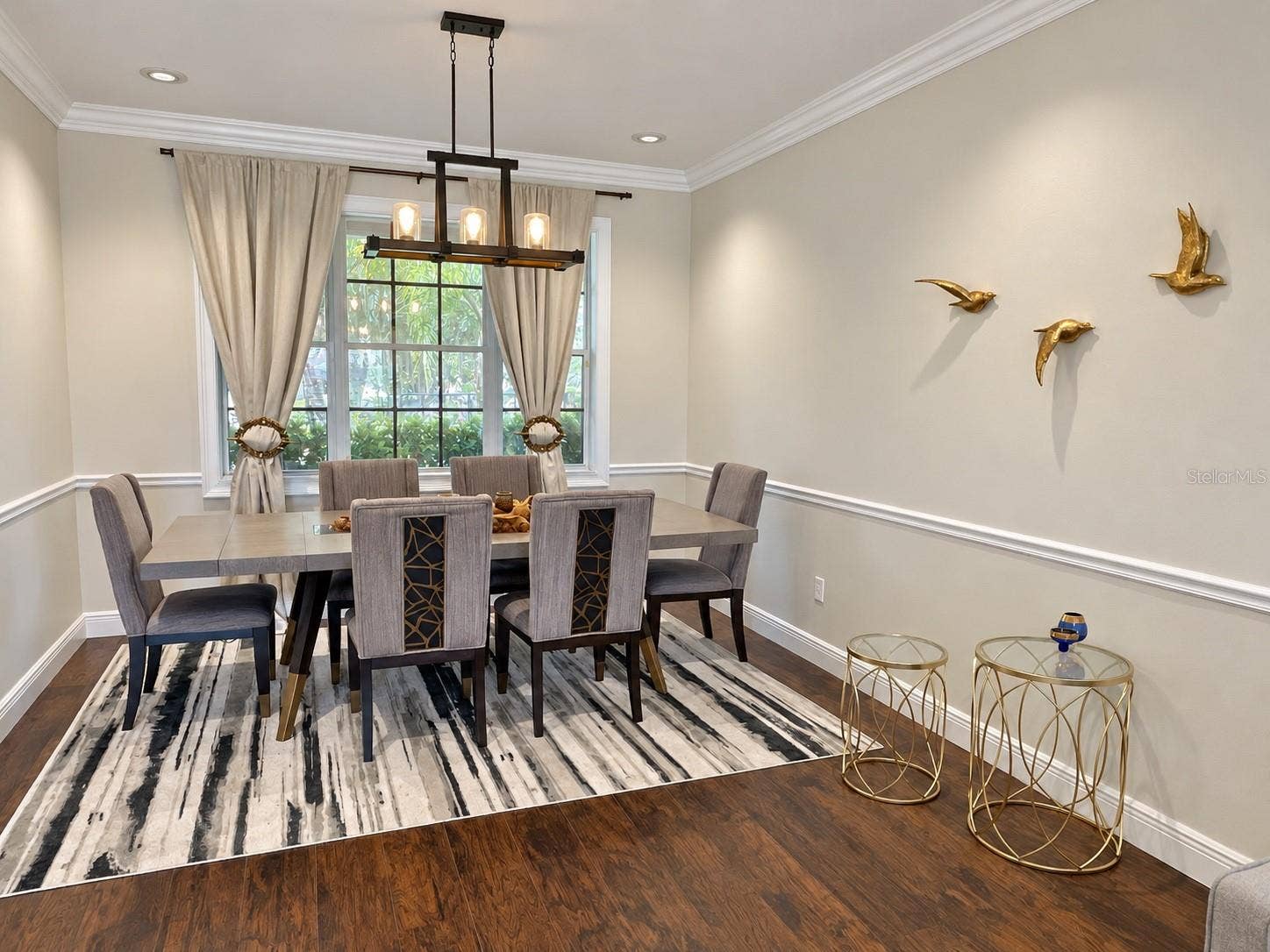 A dedicated dining area with a statement chandelier, chair-rail detailing, and crown molding. A large window adds natural light, and the adjoining living room creates a comfortable setting for entertaining.