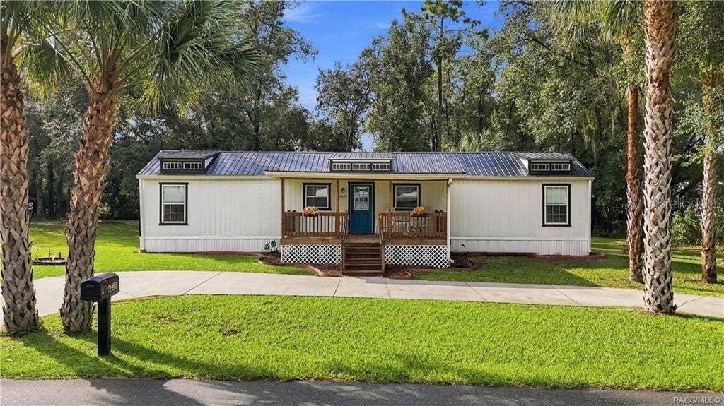 6230 W GLEN ROBBIN COURT, Crystal River, FL 34429 Welcome Home- Front Exterior Attractive home featuring a METAL ROOF, COVERED FRONT PORCH, welcoming blue front door, wooden railings & palm trees framing the property.