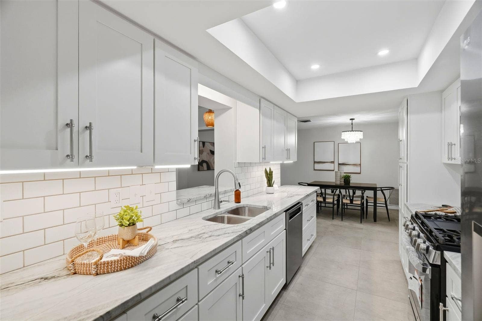 4700 14TH STREET NE, St Petersburg, FL 33703 Anchoring the home is a centrally located kitchen featuring classic white shaker-style cabinetry, a subway tile backsplash, stone countertops, and a tray ceiling with recessed lighting.