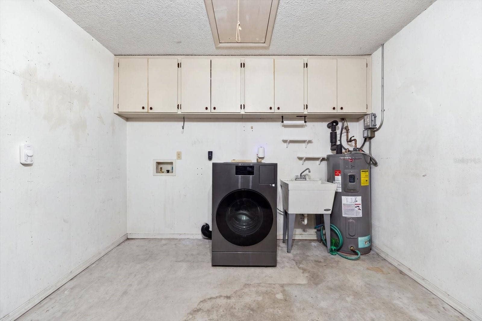 Garage with storage cabinets, washer/dryer combo, utility sink and water heater (2022). Newer Hurricane rated garage door 2023