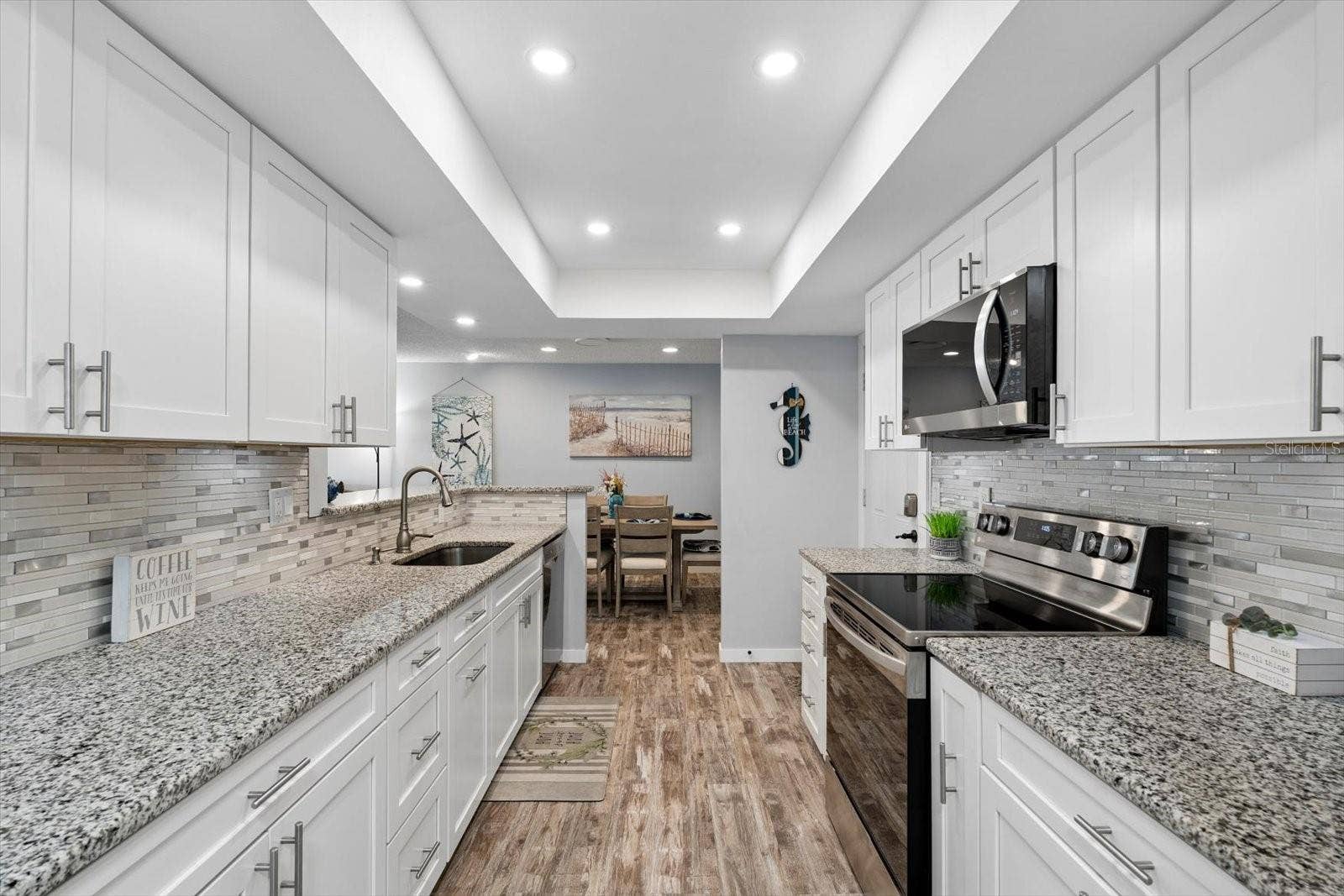 Gorgeous open kitchen with stainless steel appliances, white shaker cabinets, granite countertops, recessed lighting.