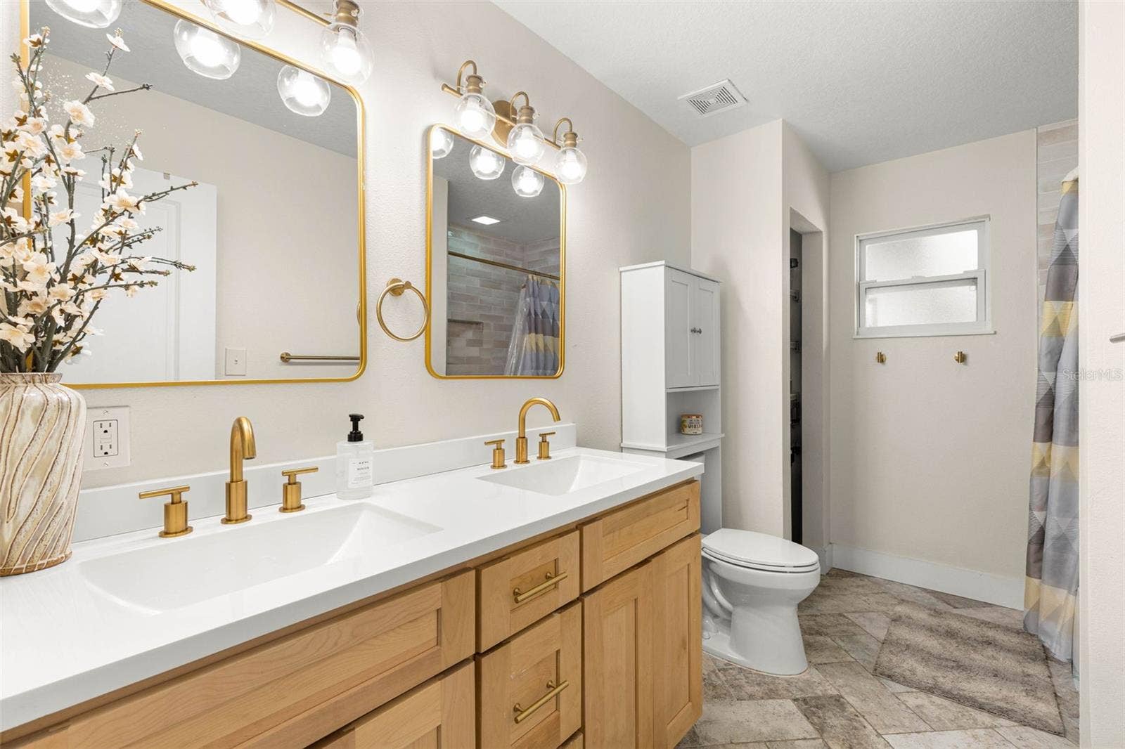 3013 GRAHAM LANE, Tampa, FL 33618 The stylish second bathroom features a double-sink vanity with natural wood cabinetry, crisp white countertops, brushed gold fixtures, coordinating mirrors, and contemporary glass-globe lighting. Neutral tile flooring and a tub/shower combination complete this thoughtfully updated space.