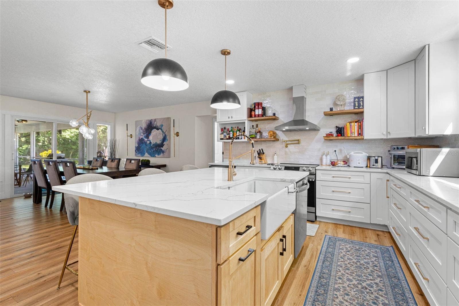 3013 GRAHAM LANE, Tampa, FL 33618 A chef-inspired kitchen with an apron-front farmhouse sink, professional-style gold faucet, convenient pot filler above the range, stainless steel range hood, and floating wood shelves. The oversized island provides additional cabinetry and generous workspace, while the open layout connects effortlessly to the dining area.