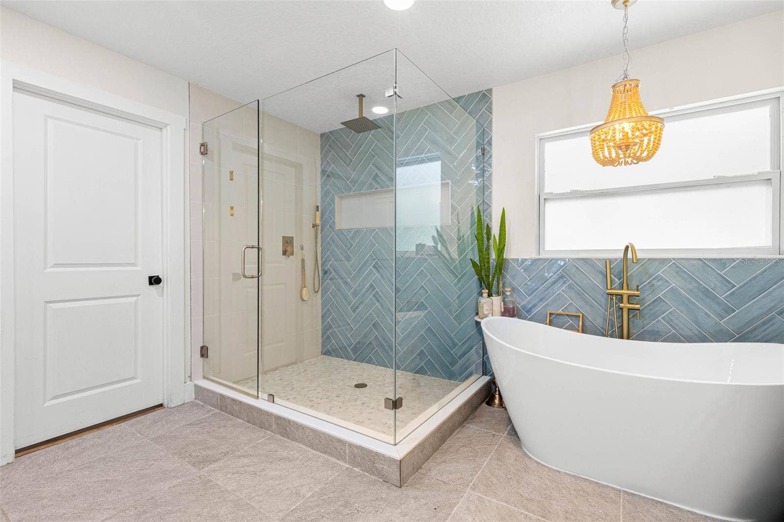 3013 GRAHAM LANE, Tampa, FL 33618 A freestanding soaking tub takes center stage beneath an elegant gold chandelier, complemented by a floor-mounted gold tub filler and beautiful blue-green herringbone tile. The adjoining glass-enclosed shower completes this luxurious, spa-inspired retreat.