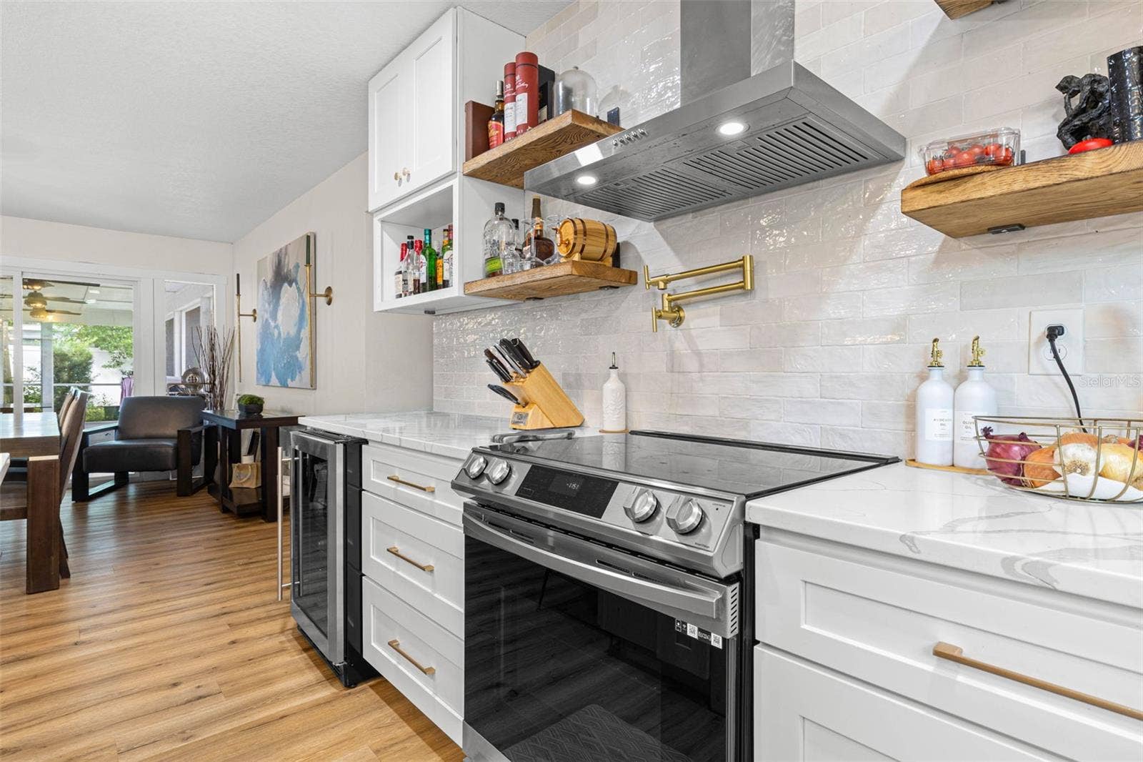 3013 GRAHAM LANE, Tampa, FL 33618 A closer look at the kitchen's stylish cooking area reveals a stainless steel smooth-top range, contemporary vent hood, convenient gold pot filler, textured subway tile backsplash, and floating wood shelves. Quartz countertops and white shaker cabinetry with gold hardware complete this beautifully coordinated space.