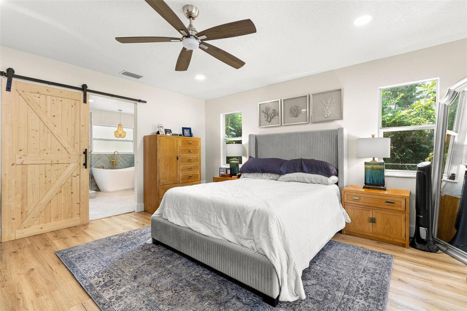 3013 GRAHAM LANE, Tampa, FL 33618 The inviting primary suite features beautiful wood-look luxury vinyl flooring, recessed lighting, a contemporary ceiling fan, and windows overlooking the greenery outside. A rustic sliding barn door adds architectural character while opening to the beautifully appointed ensuite bathroom.
