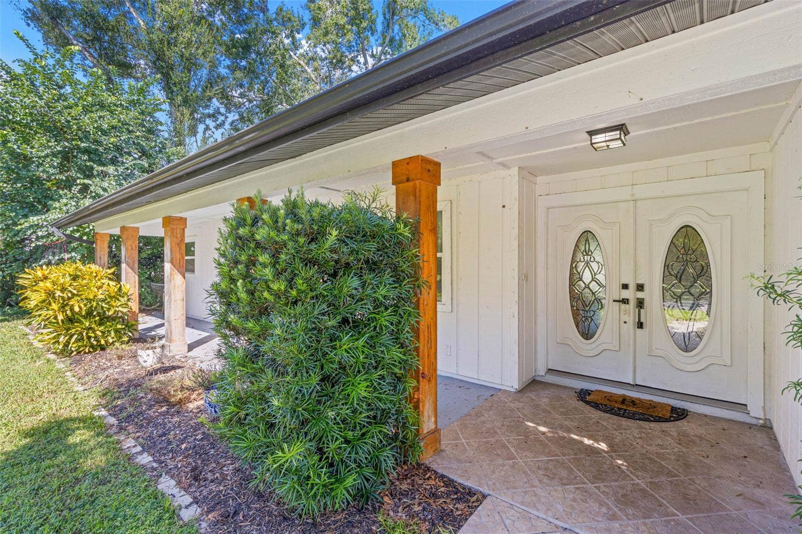 3013 GRAHAM LANE, Tampa, FL 33618 A closer look at the inviting covered front porch, featuring tiled flooring, natural wood columns, decorative double entry doors with oval glass inserts, and thoughtfully placed landscaping.