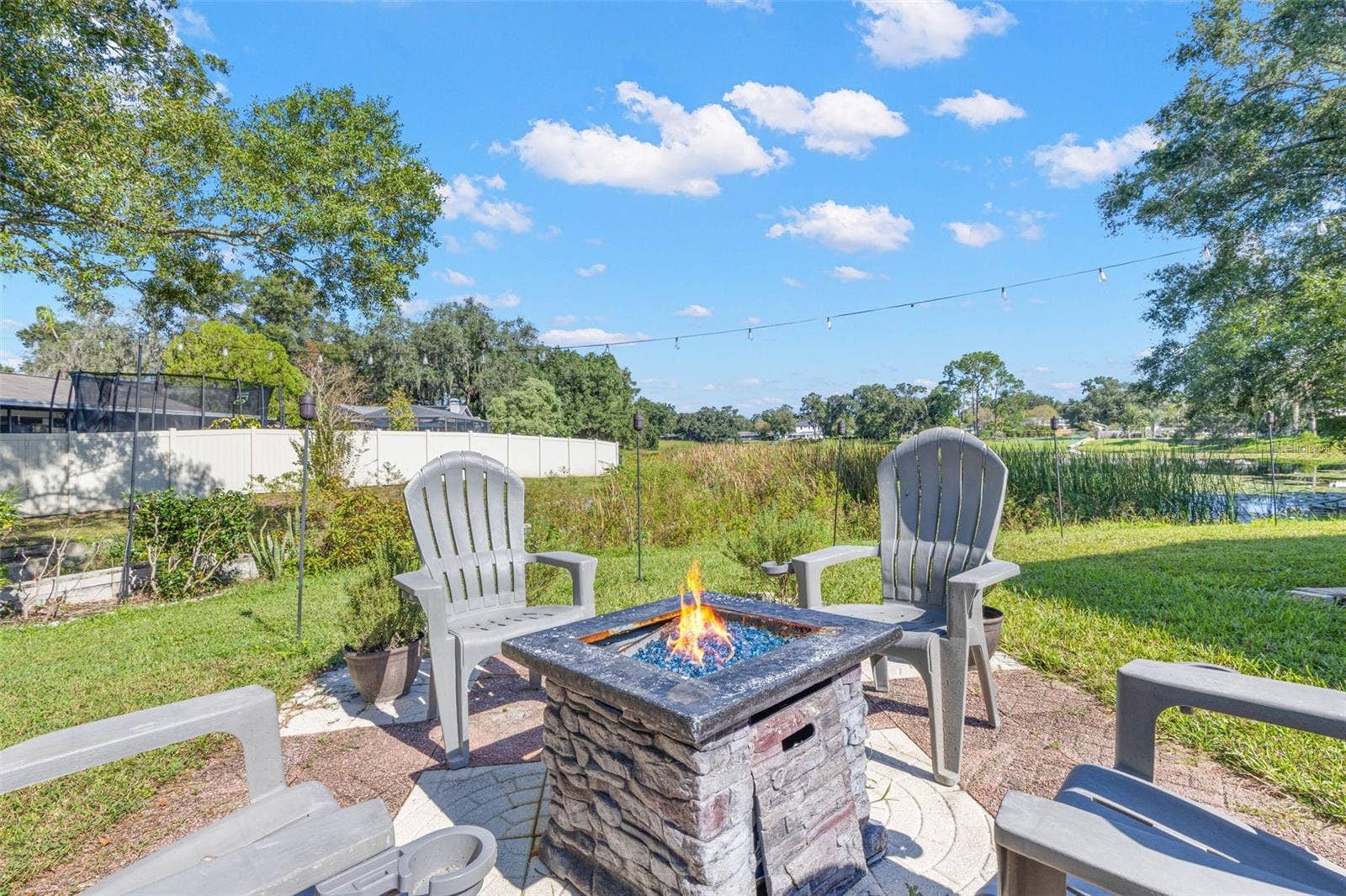 3013 GRAHAM LANE, Tampa, FL 33618 Imagine relaxing evenings under the stars in this inviting backyard retreat! A stone-look fire pit anchors the outdoor gathering area, while overhead string lighting and a peaceful pond backdrop create a charming setting for entertaining.