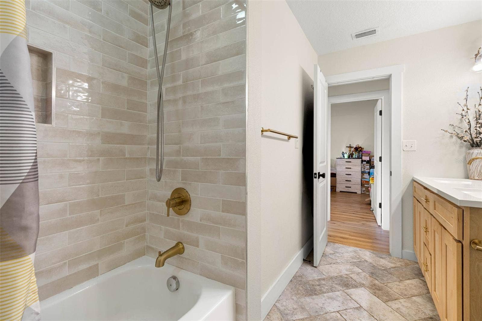 3013 GRAHAM LANE, Tampa, FL 33618 The second bathroom's tub/shower combination features glossy, neutral-toned subway tile, a recessed storage niche, and brushed gold fixtures, including a convenient handheld showerhead. Coordinating tile flooring and warm wood cabinetry complete the updated space.