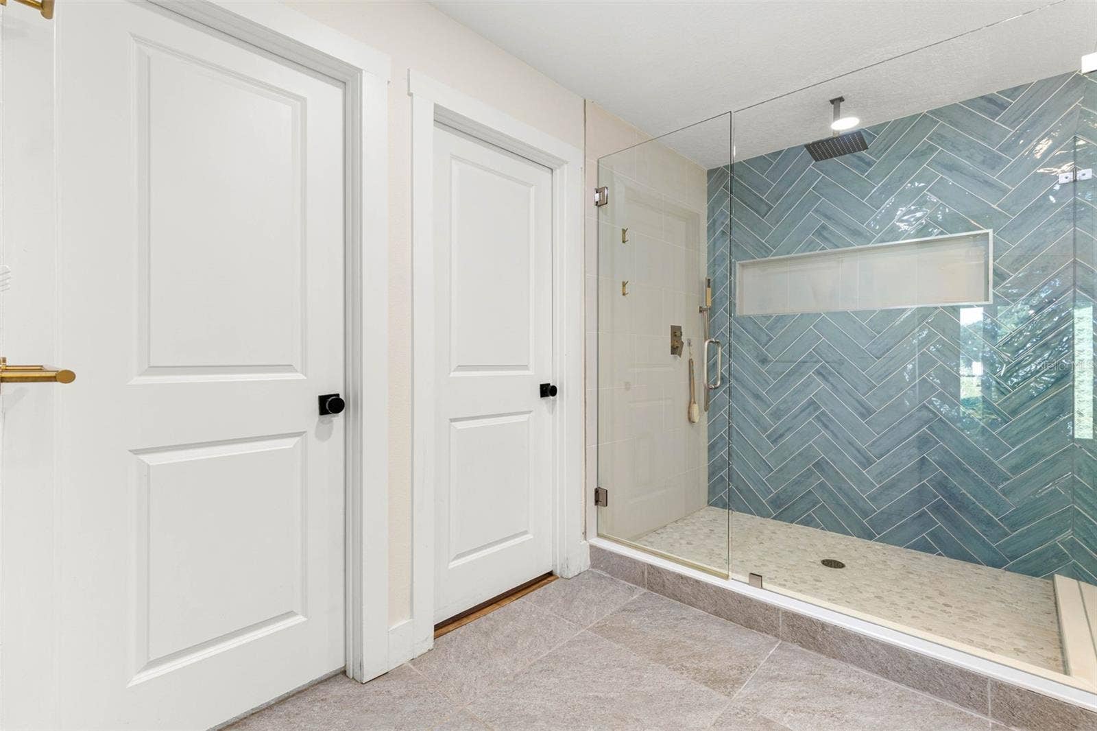 3013 GRAHAM LANE, Tampa, FL 33618 The primary bathroom's oversized walk-in shower features a frameless glass enclosure, striking blue-green herringbone tile, a rainfall showerhead, built-in recessed niche, and a pebble-style tile floor. A beautiful combination of contemporary design and everyday functionality.