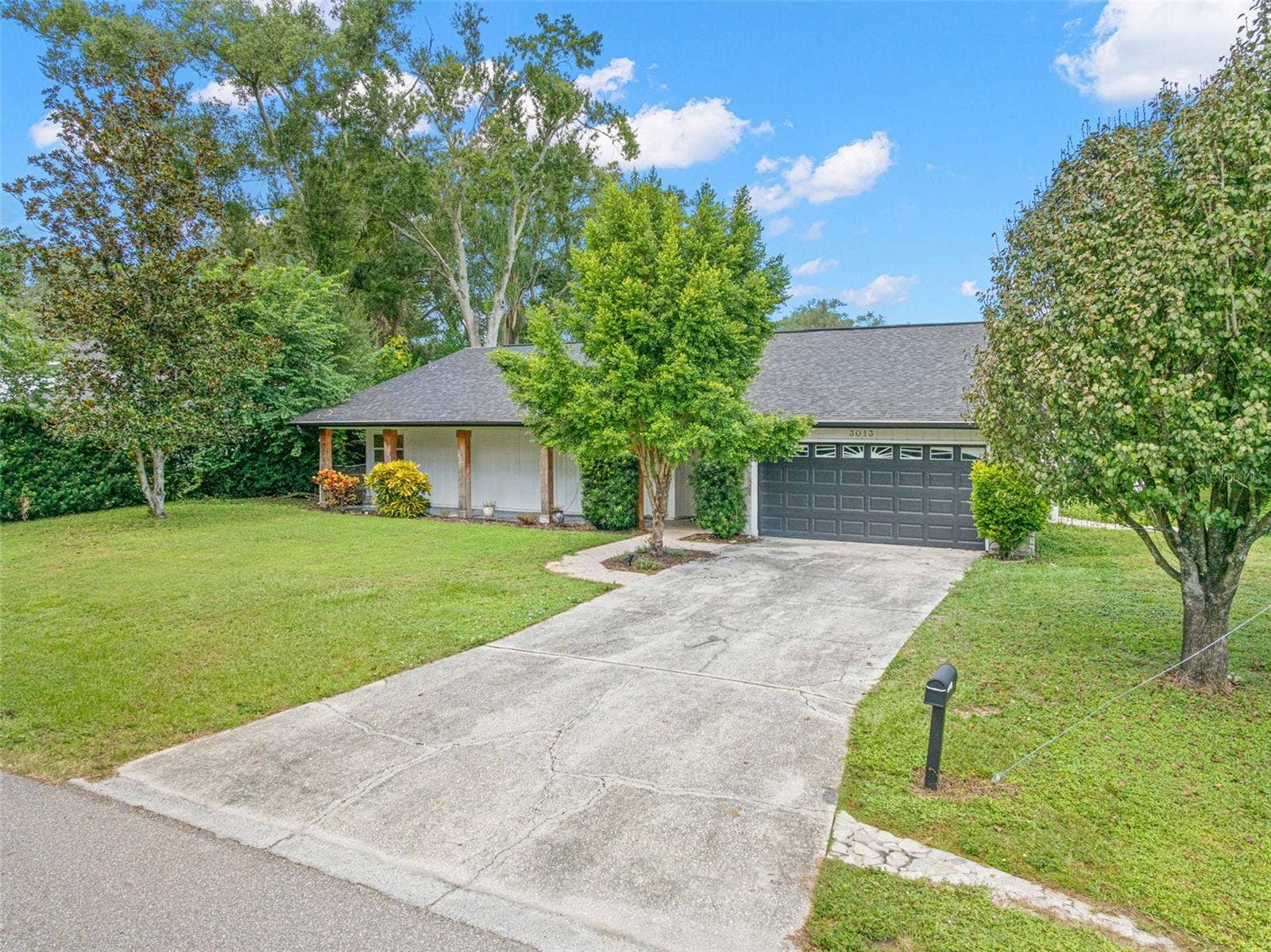 3013 GRAHAM LANE, Tampa, FL 33618 A wide concrete driveway leads to the attached two-car garage, offering convenient parking and additional storage. Mature shade trees, lush greenery, and an expansive front lawn enhance the home's curb appeal.