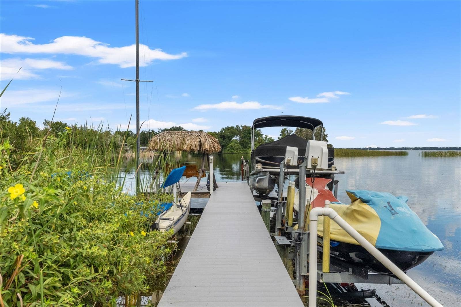 Your Florida boating lifestyle starts right here! The waterfront dock features a covered pontoon boat on a lift, personal watercraft lift, and space for additional recreational equipment. A thatched-roof seating area at the end of the dock offers a relaxing spot overlooking the lake.