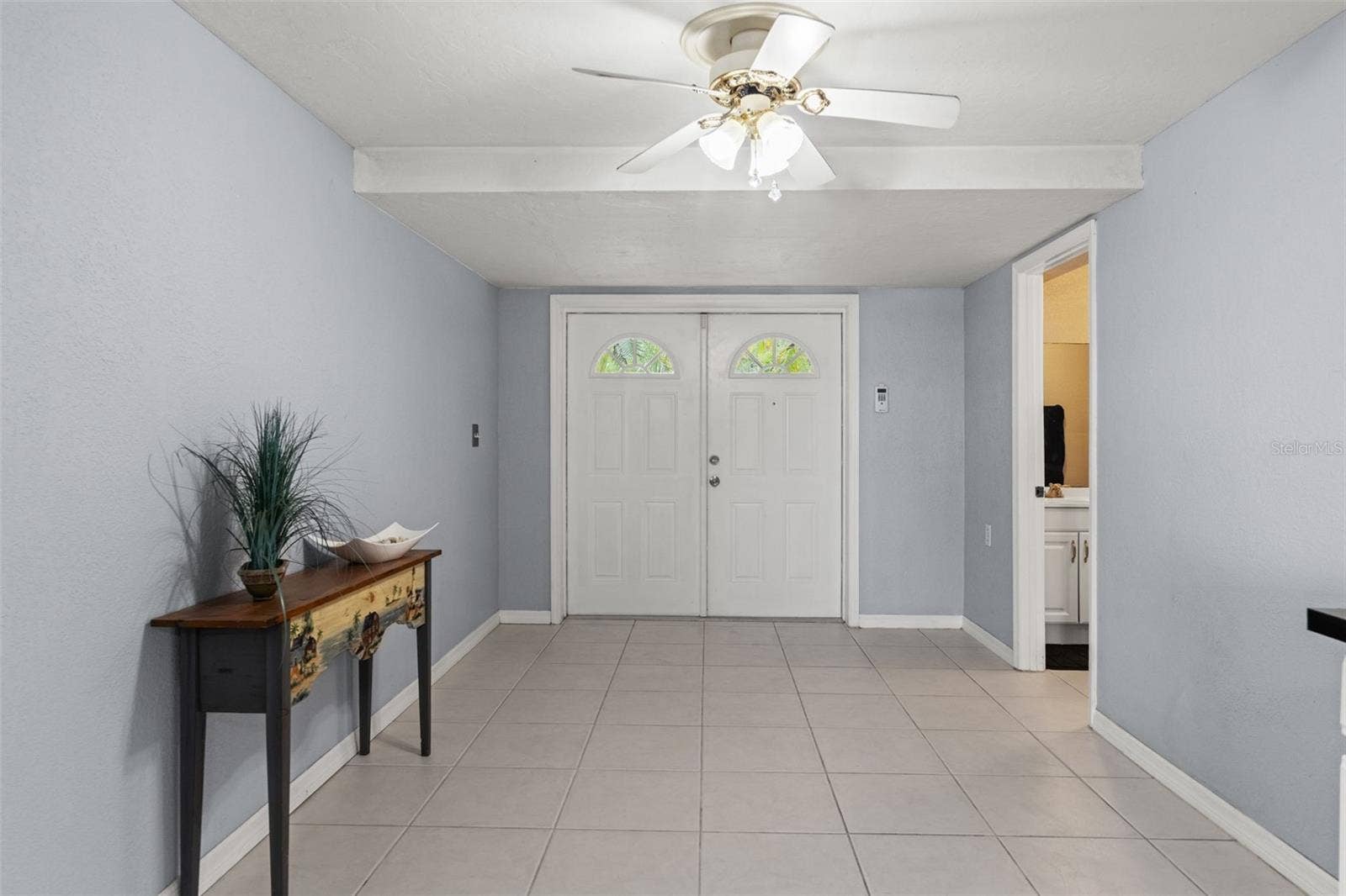 Double entry doors welcome you into the home's lower level, where neutral tile flooring, light-colored walls, and ceiling fans create a versatile space. With its own exterior entrance and nearby bathroom, this level offers flexibility for a variety of household needs.