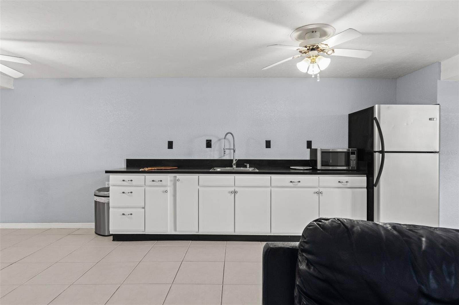 A closer look at the lower-level kitchenette reveals generous cabinet storage, dark countertops, a stainless-steel sink, refrigerator, and microwave. This additional food preparation area makes it easy to accommodate guests or enjoy snacks and refreshments without heading upstairs.