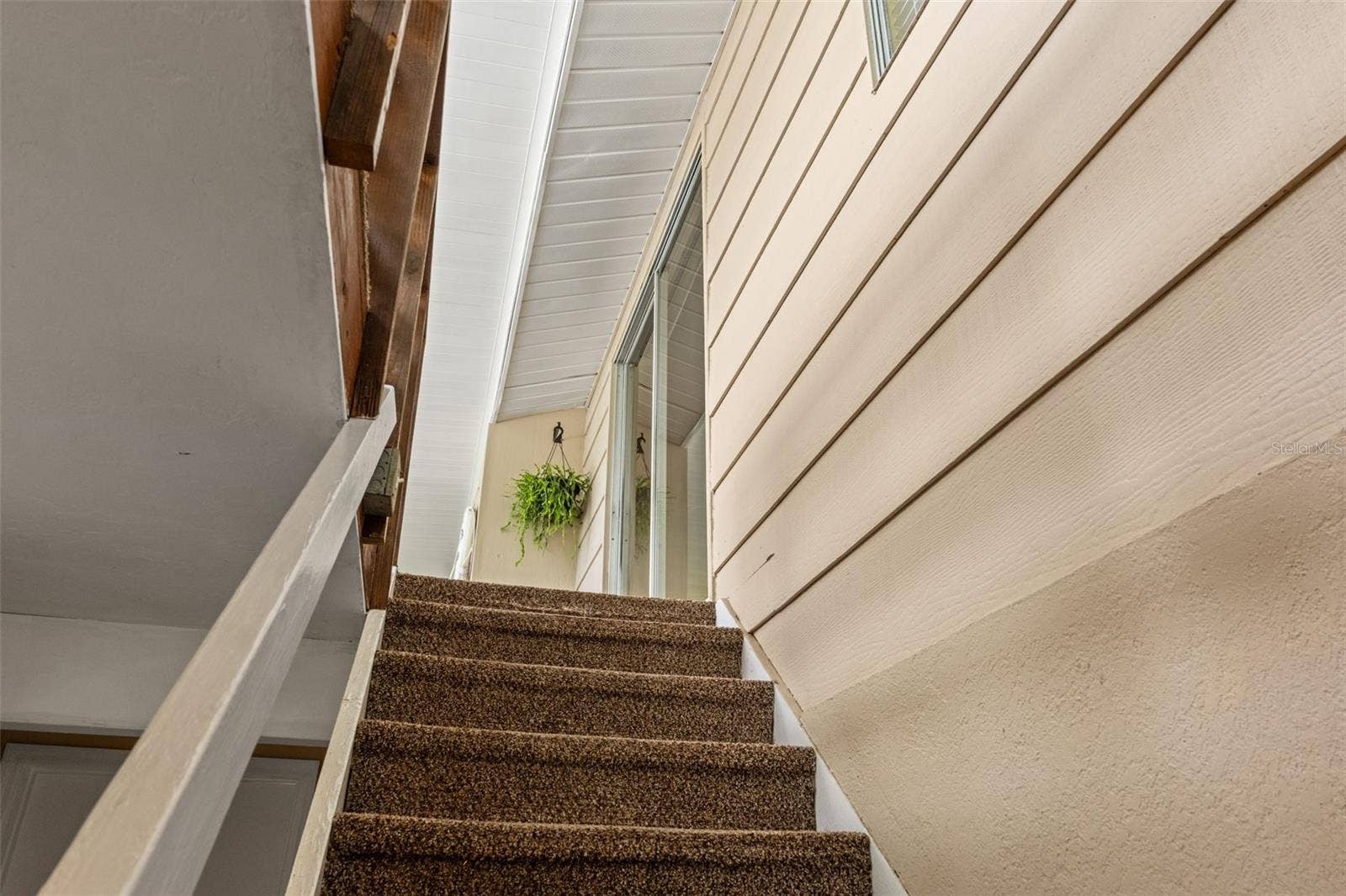 A carpeted stairway connects the elevated upper living area with the lower level. This view highlights the home's distinctive two-level design and access to the screened upper porch.