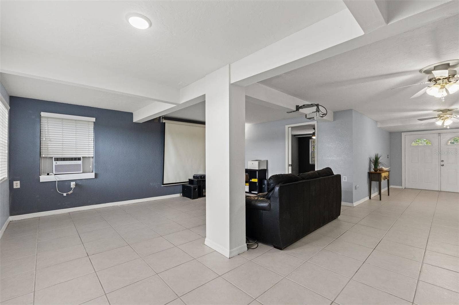 This wide-angle view highlights the versatility of the downstairs layout, with an open area adjoining the media room and easy access to the separate exterior entrance. Tile flooring runs throughout, providing a practical foundation for entertaining, recreation, or additional living space.