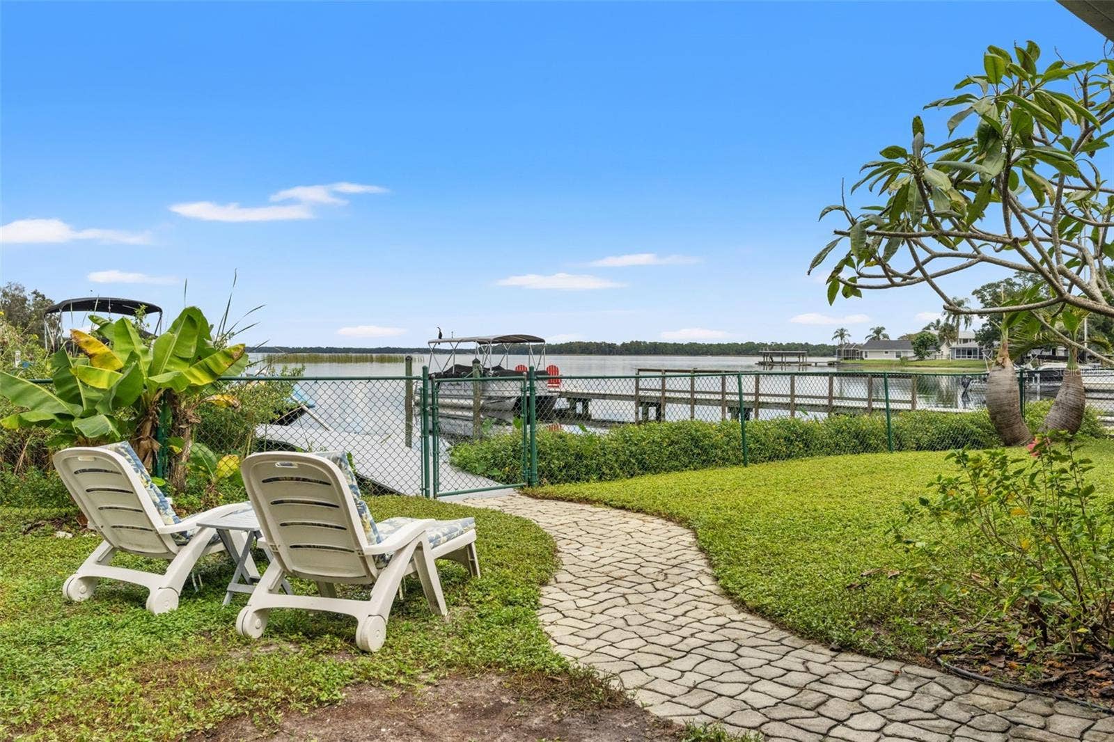 Pull up a lounge chair and enjoy the view! A paver walkway connects the backyard seating area to the waterfront gate and dock. With tropical landscaping, open water, and boats nearby, this setting captures the appeal of Florida lakefront living.