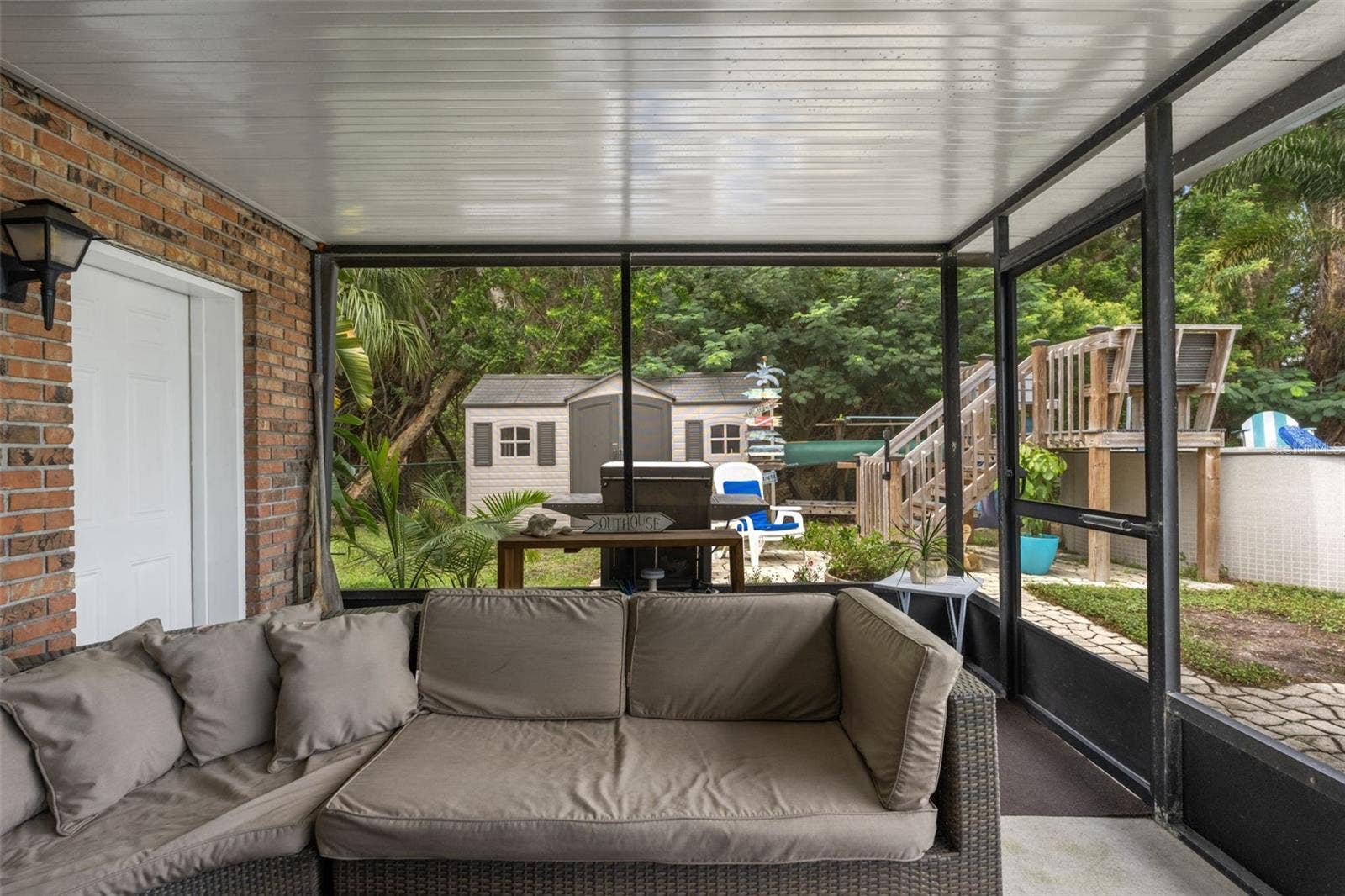 This covered, screened patio provides another comfortable outdoor gathering area, complete with sectional seating and access to the backyard. Beyond the enclosure, discover an above-ground pool, outdoor grilling area, and storage shed surrounded by mature trees.