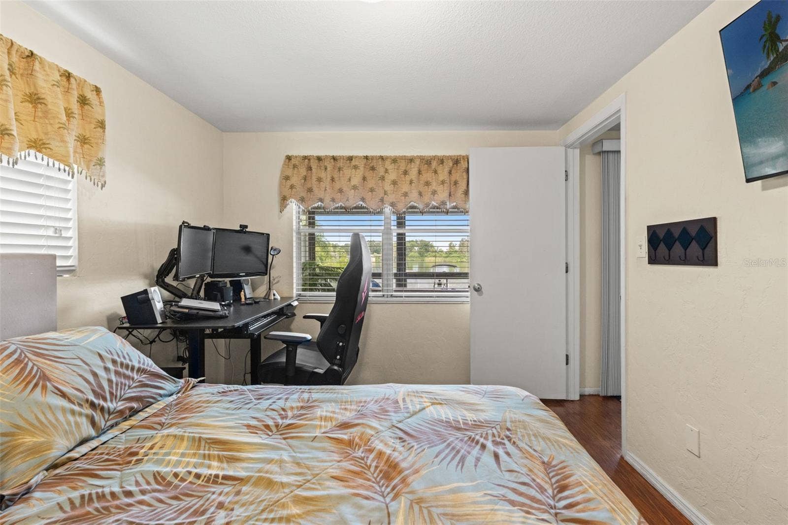 This versatile bedroom offers wood flooring, two windows for natural light, and a built-in closet. Currently arranged with both a bed and computer workstation, it demonstrates how easily the room accommodates sleeping and home office needs.