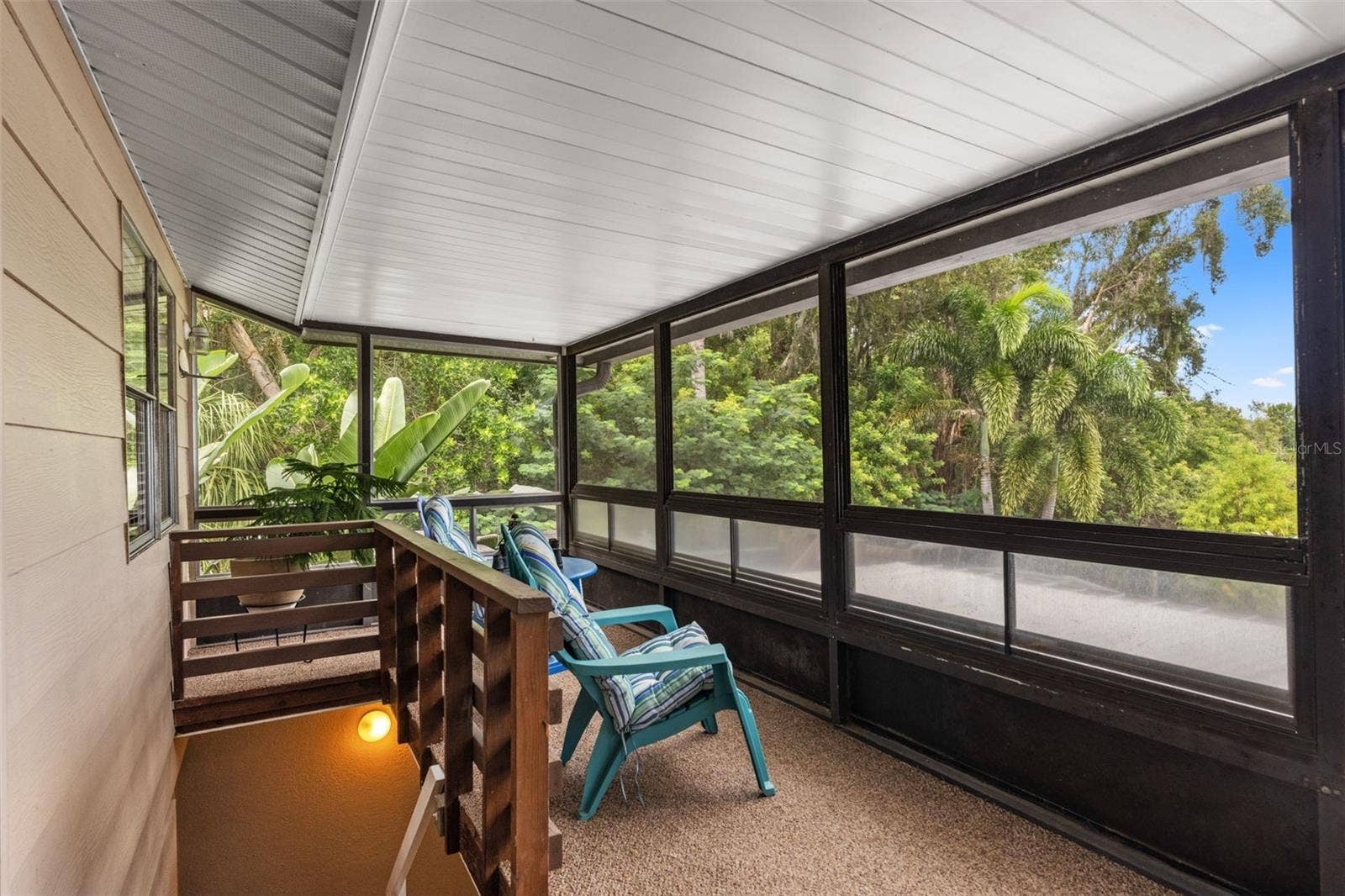 Your own peaceful escape among the palms! This elevated screened porch offers comfortable seating, lush tropical views, and a covered setting for enjoying Florida's beautiful weather. A staircase provides access to the lower level.