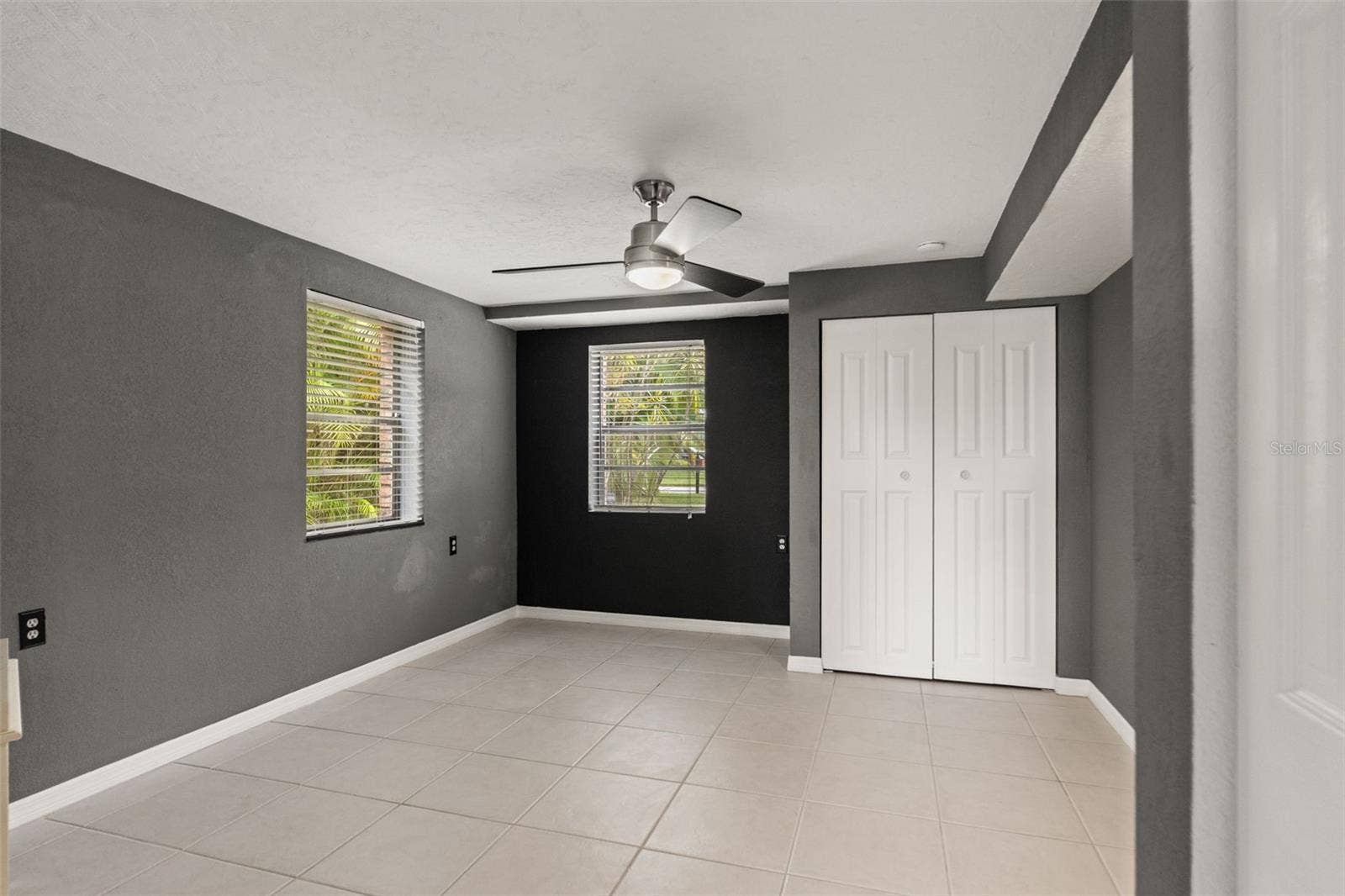 This separate downstairs room features neutral tile flooring, contemporary ceiling fan, two windows, and a closet. Its flexible layout provides options for a home office, hobby room, or additional guest space, depending on your needs.