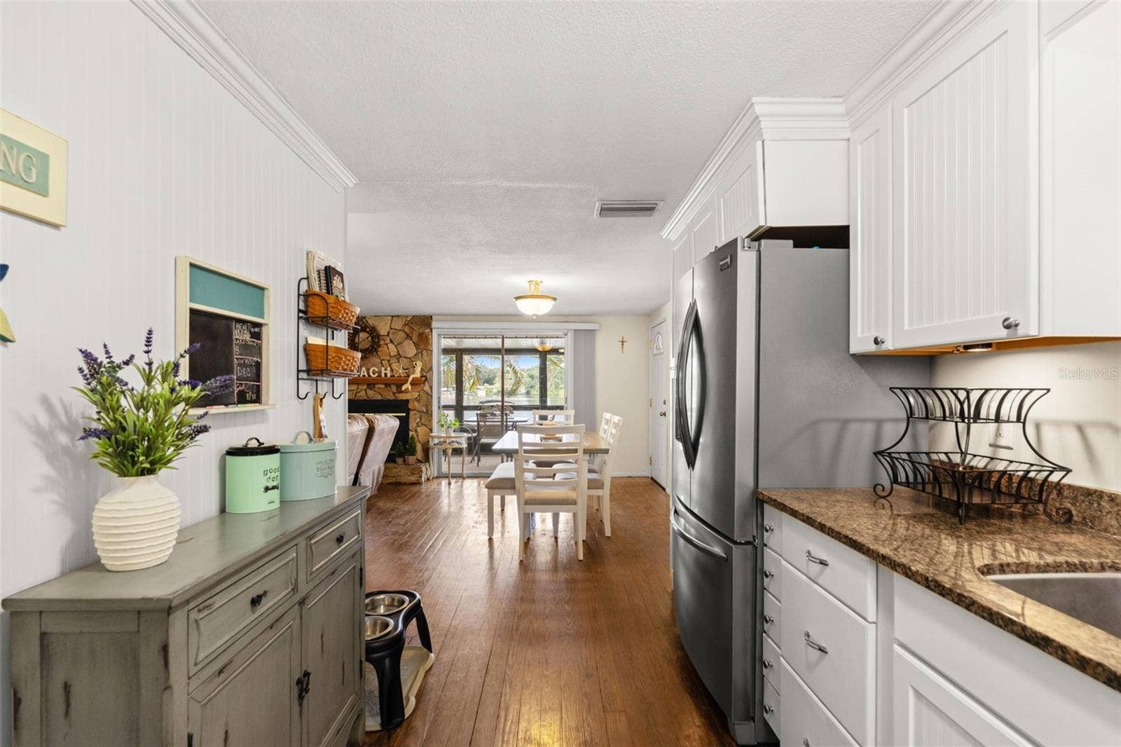 The kitchen opens directly to the dining and living areas, creating an easy flow throughout the upper level. White cabinetry, warm wood flooring, and a stainless steel refrigerator complement the home's relaxed coastal character.