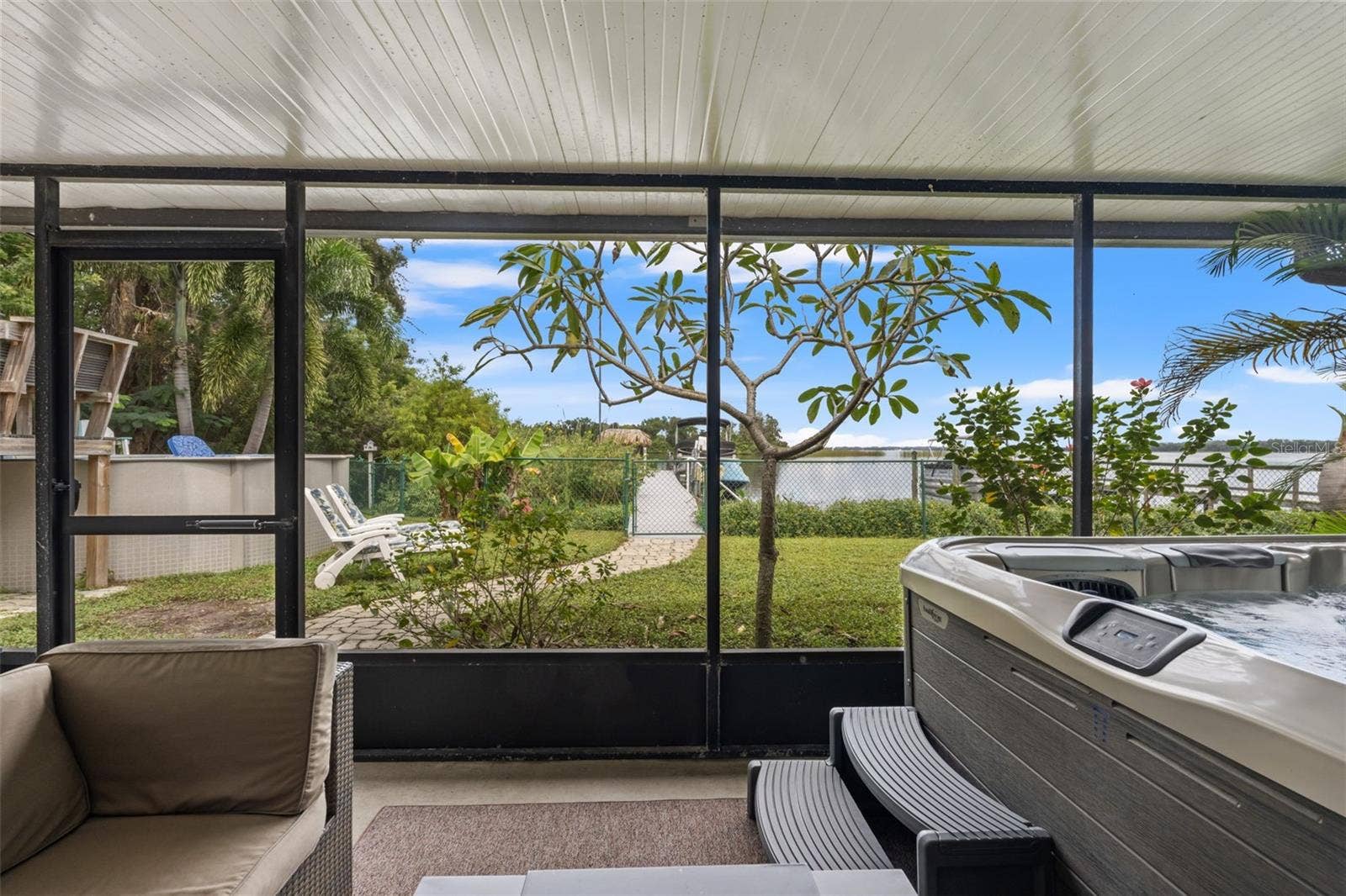 The lower-level screened patio overlooks a grassy backyard with a pathway leading toward the waterfront. Enjoy views of the dock and boats beyond, with additional outdoor recreation space just steps away.