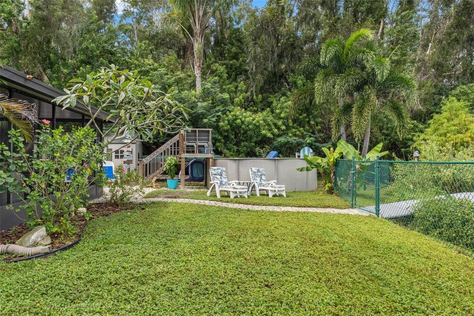 Enjoy your own backyard retreat with an above-ground pool, raised wooden deck, and surrounding lounge areas. Mature trees and tropical landscaping create a leafy backdrop, while the nearby lawn and paver walkway provide space to enjoy the outdoors.