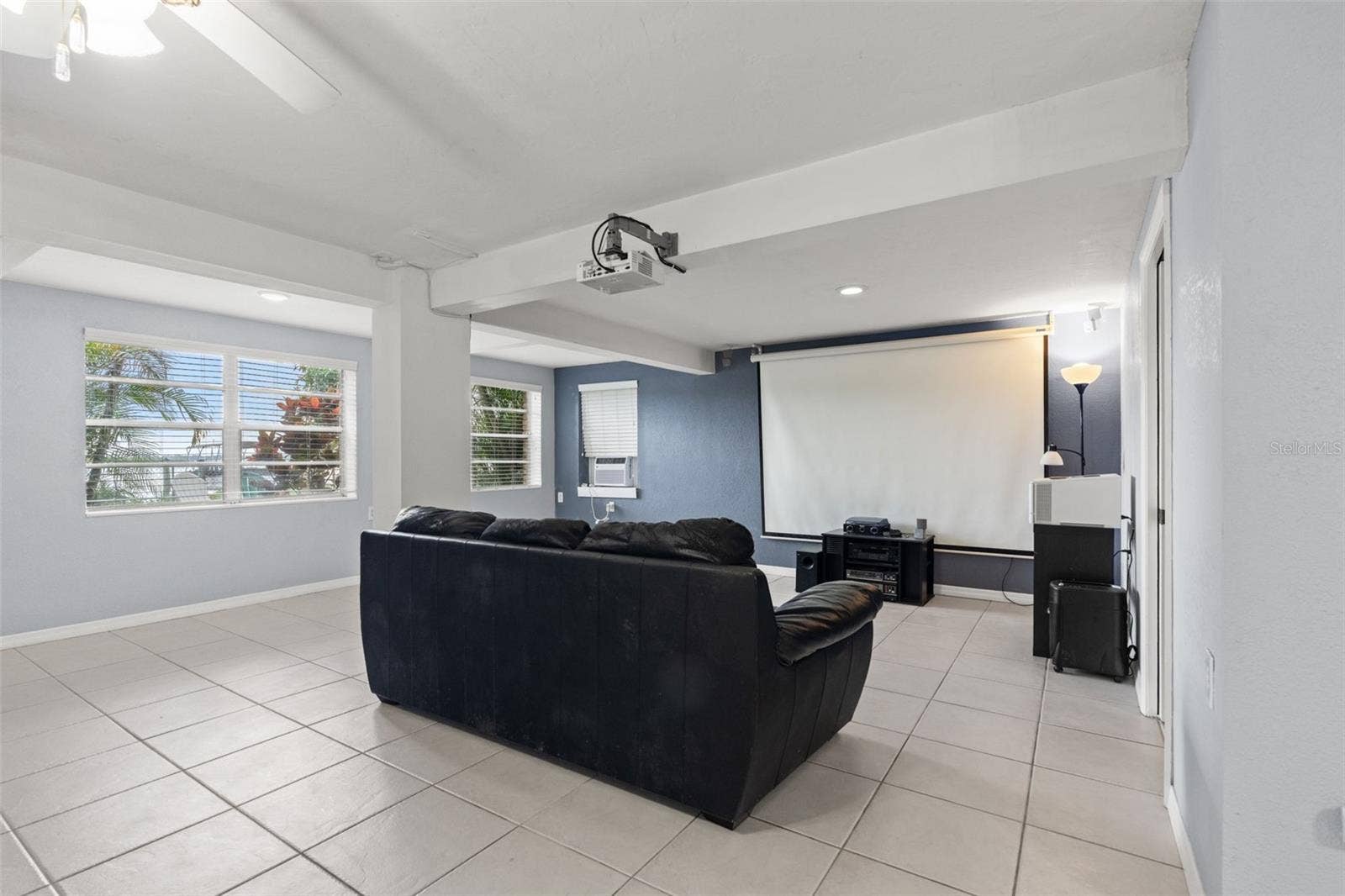 Movie nights have their own dedicated space! The lower-level living area is currently arranged as a home theater, complete with a large projection screen, ceiling-mounted projector, and comfortable seating. Multiple windows bring natural light into the room, making it equally suitable for everyday relaxation.