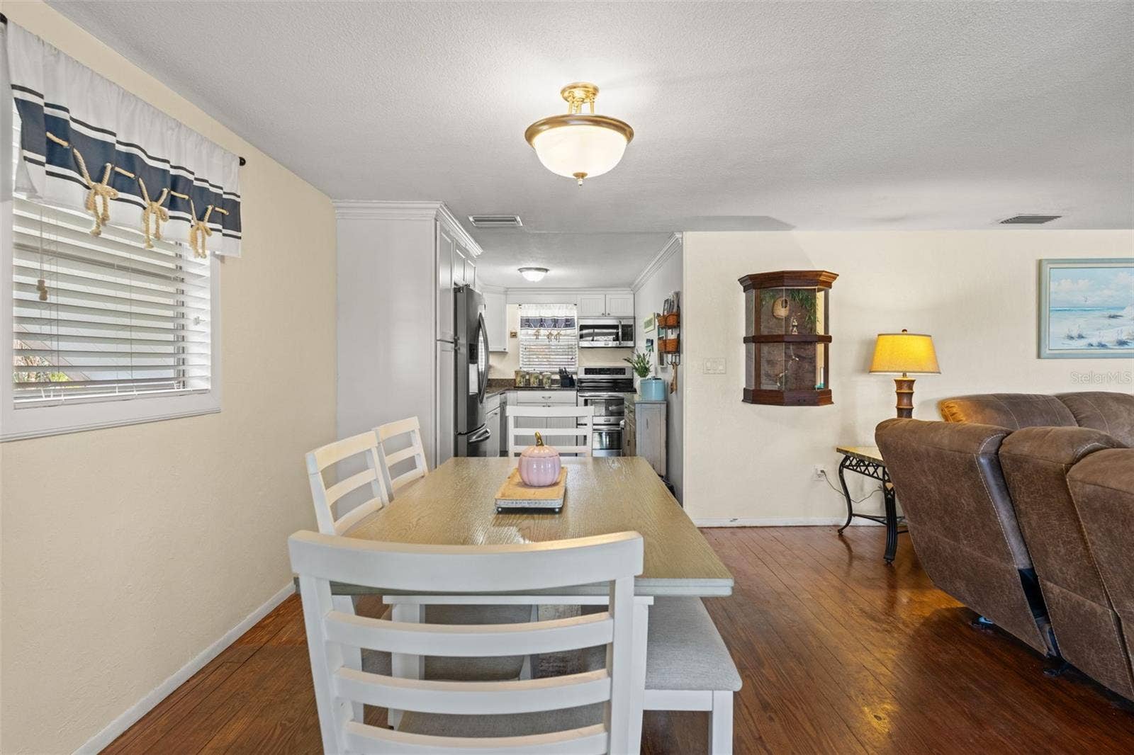 The dining area sits conveniently between the kitchen and living room, making meals and gatherings easy. Wood flooring, soft neutral walls, and natural light create a comfortable, welcoming atmosphere.