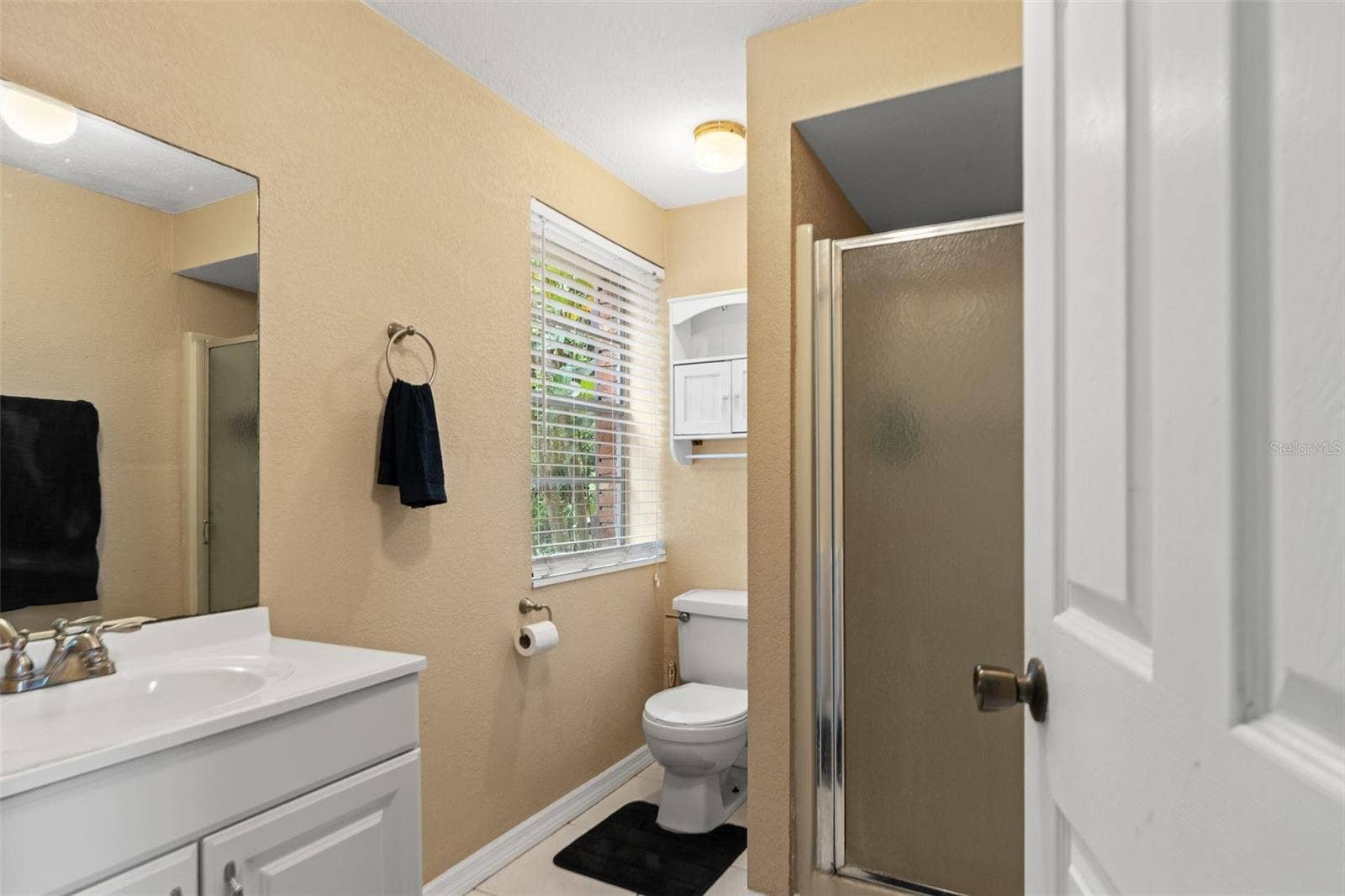 This lower-level bathroom features a white vanity, a walk-in shower with frosted glass enclosure, and a window that welcomes natural light. Conveniently located near the kitchenette and living area, it adds functionality to the home's flexible downstairs layout.