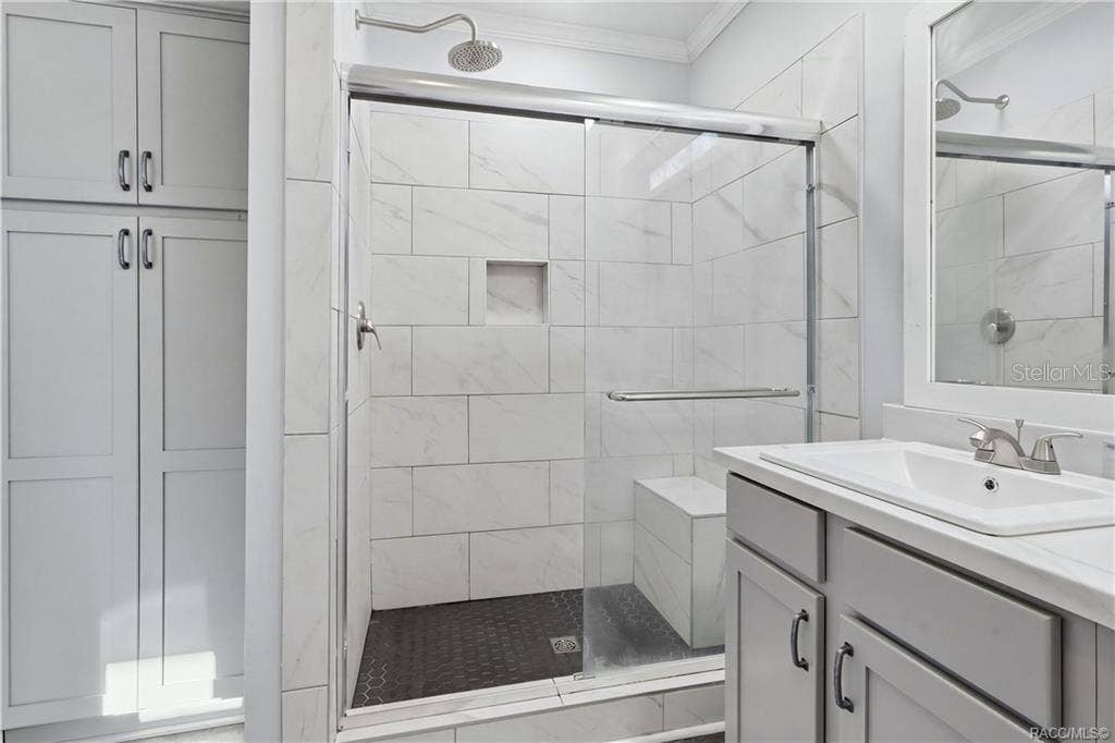 7528 N CHABAUD TERRACE, Crystal River, FL 34428 WALK-IN SHOWER features marble-look tile, a rainfall-style showerhead, glass sliding doors, built-in seating & a convenient recessed niche.
