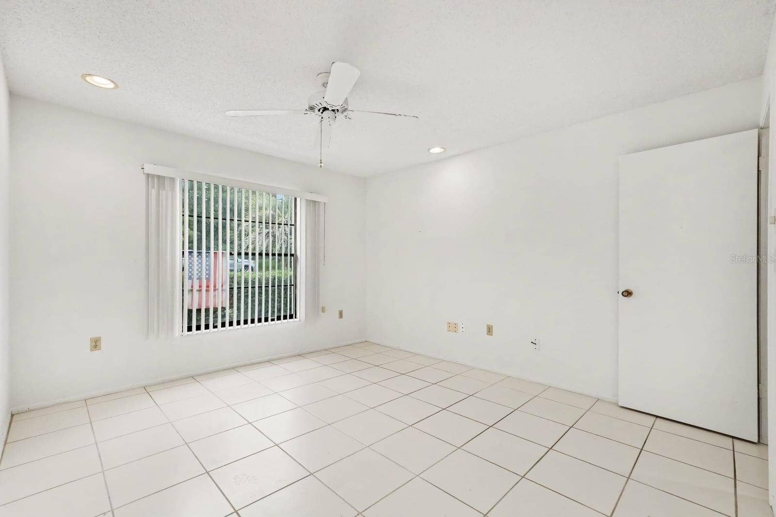Bright Bedroom with Tile Flooring and Vertical Blinds Overlooking Yard