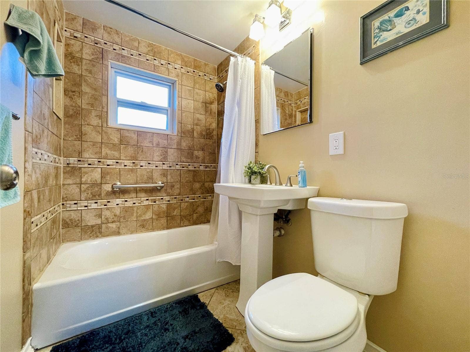 Full bathroom accented by floor-to-ceiling wall tiles, a classic pedestal sink, and a combination bathtub and shower.
